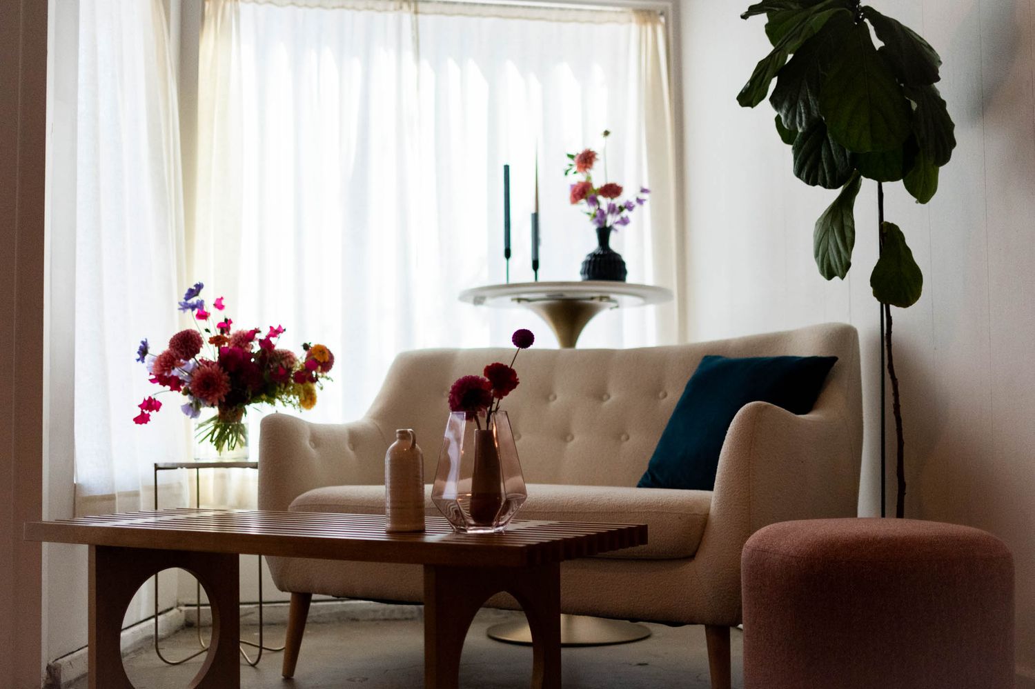 Cozy living room corner with beige sofa, red floral arrangements and sheer curtains.