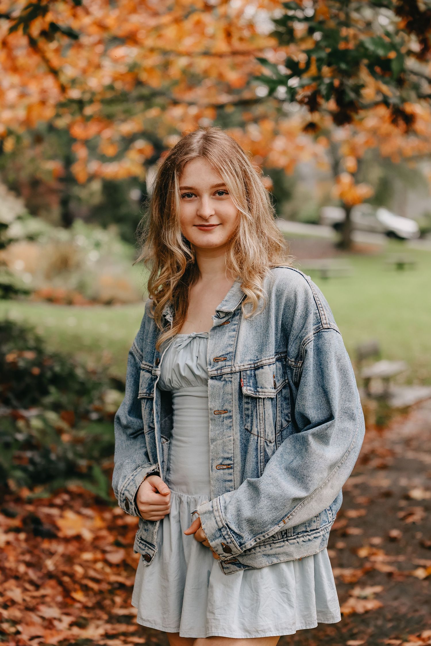 Autumn portrait in a park with orange leaves featuring denim jacket and gray dress styling.