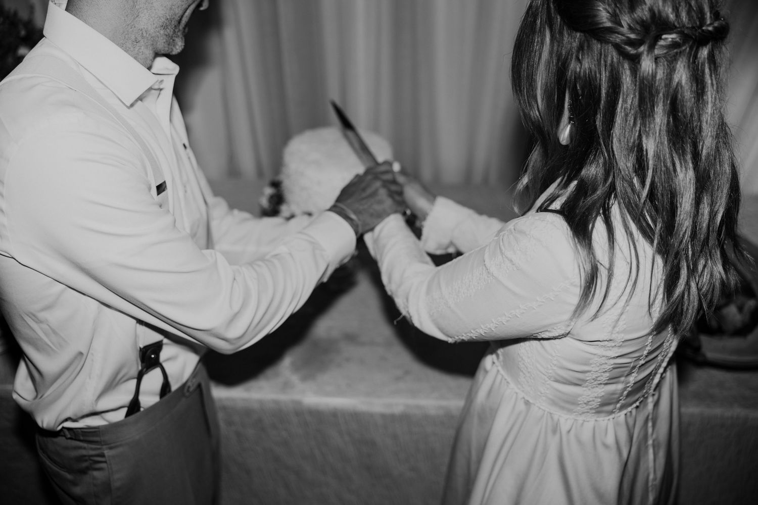 A couple holds hands during a dance, captured in intimate black and white photography.