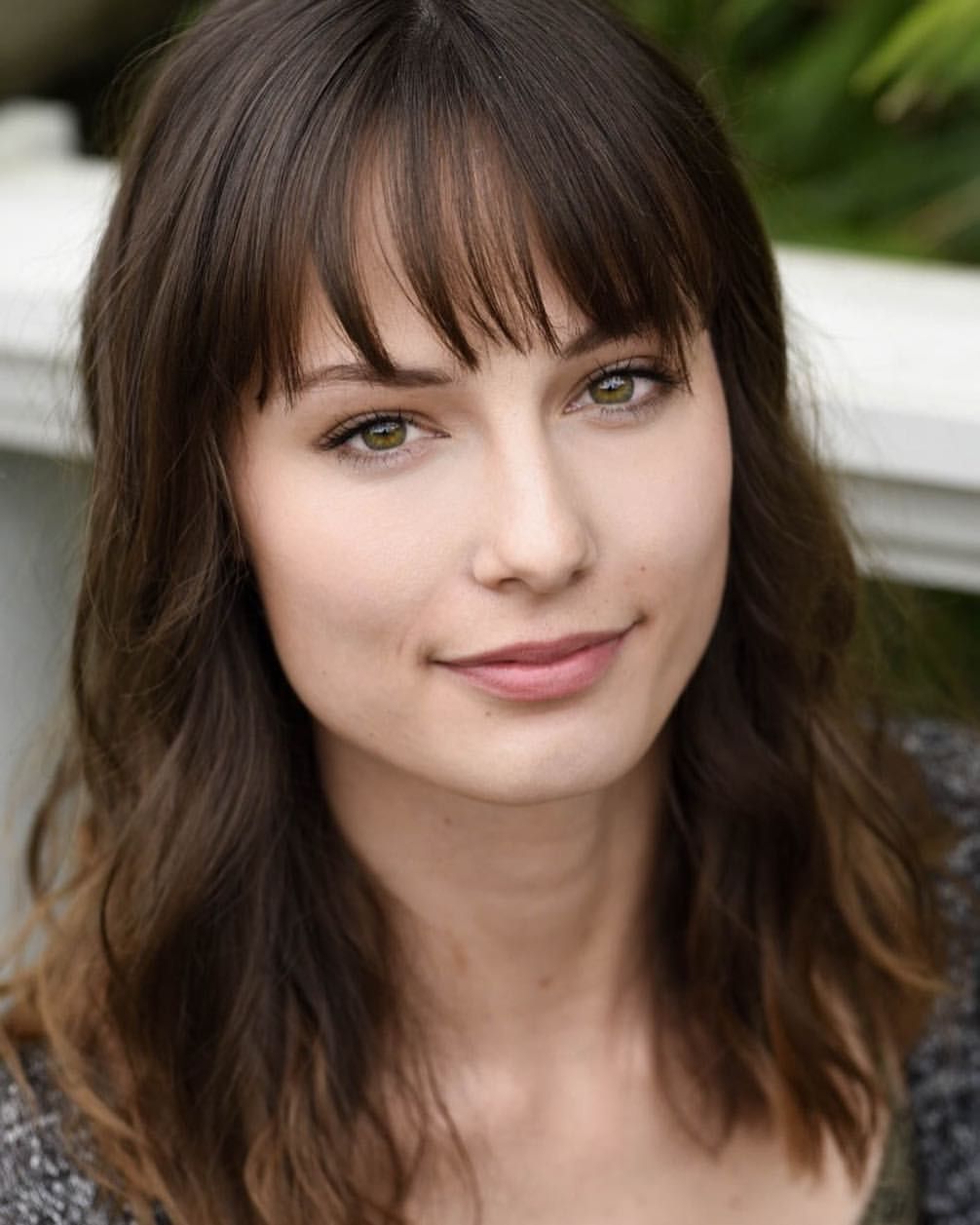 Professional headshot with bangs and natural makeup against light background.