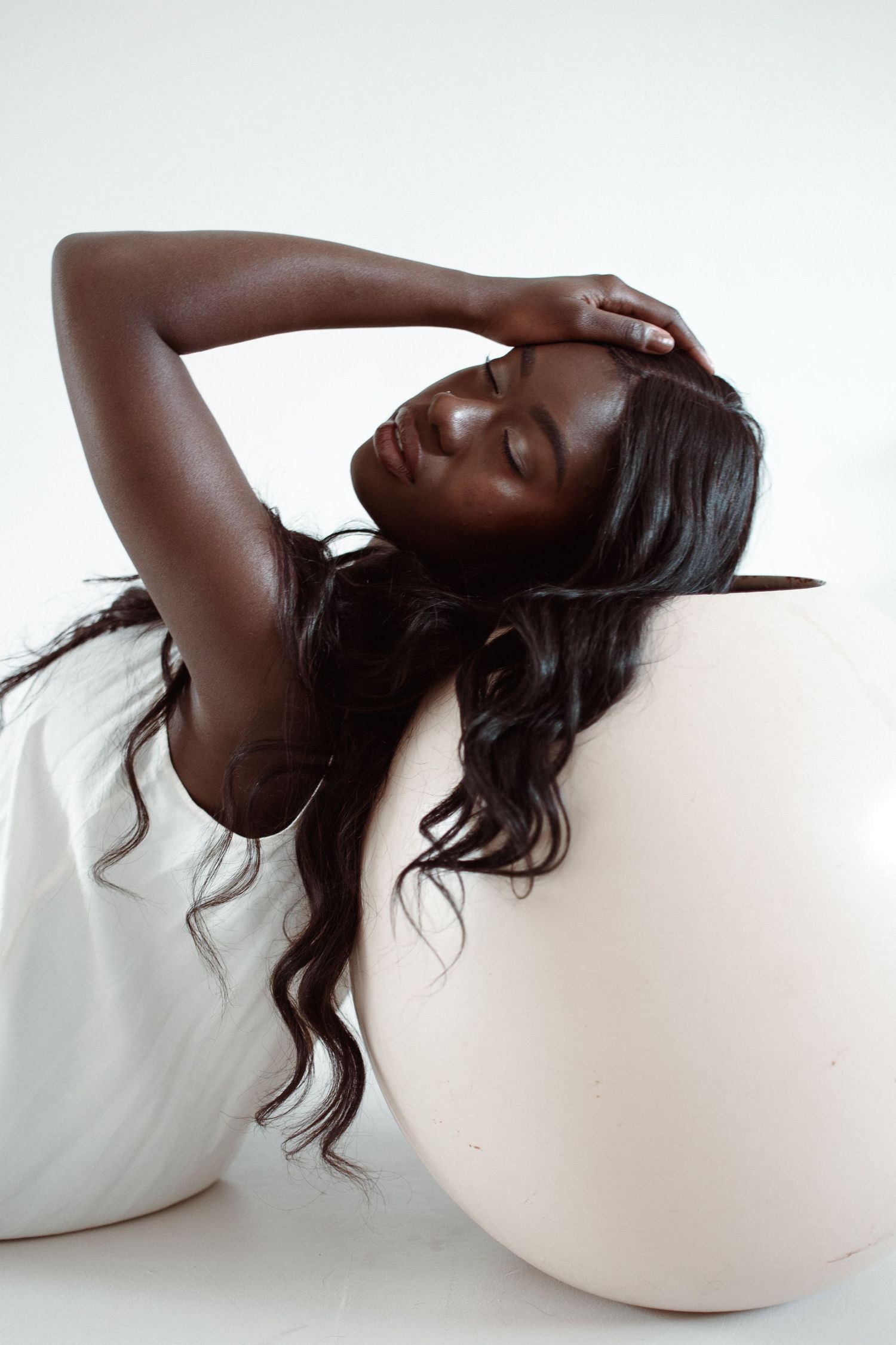 Artistic fashion portrait with long wavy hair and white top against minimalist background.