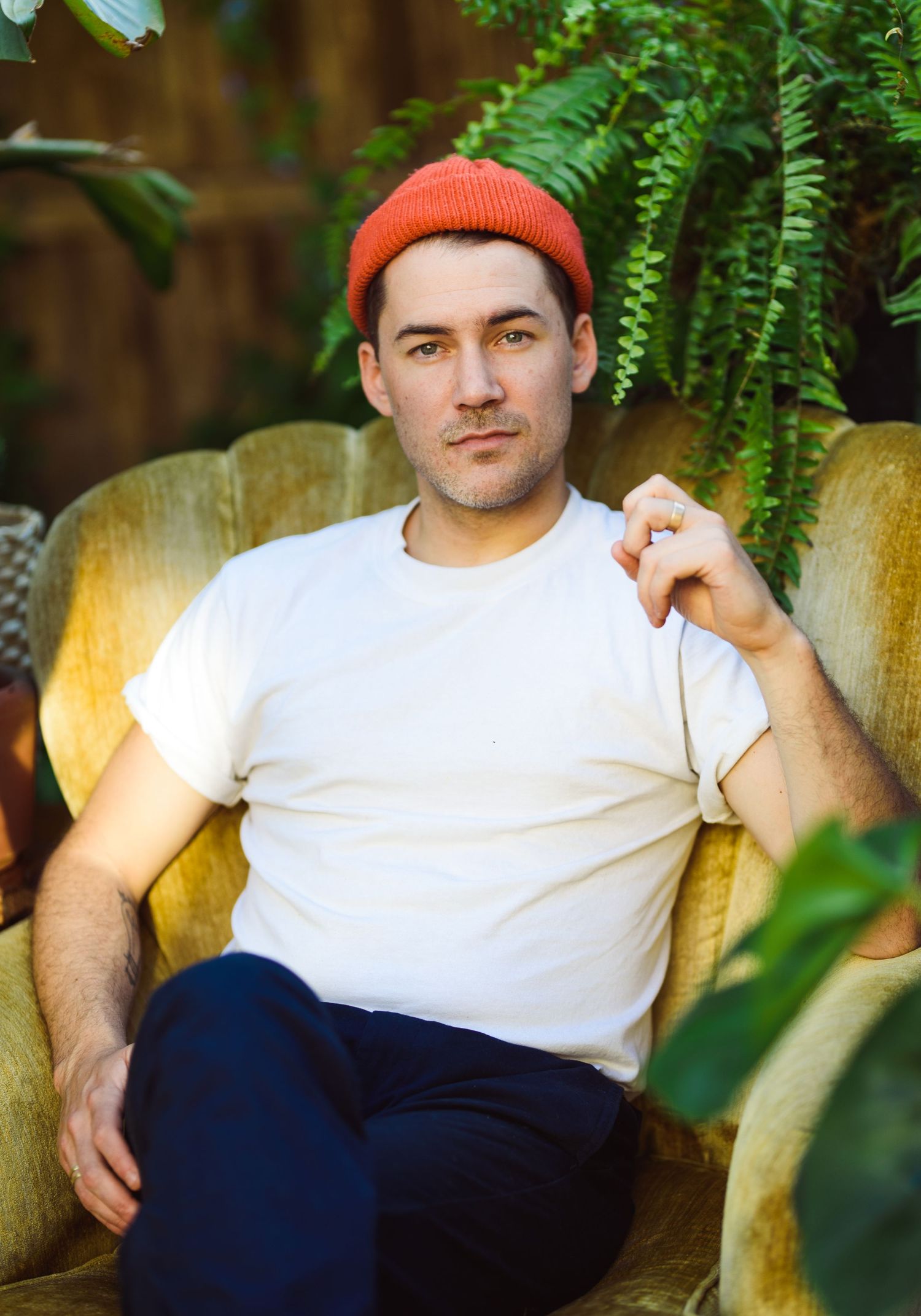 A series of outdoor portraits showing someone in a white t-shirt and navy pants posing against greenery and a wooden fence.