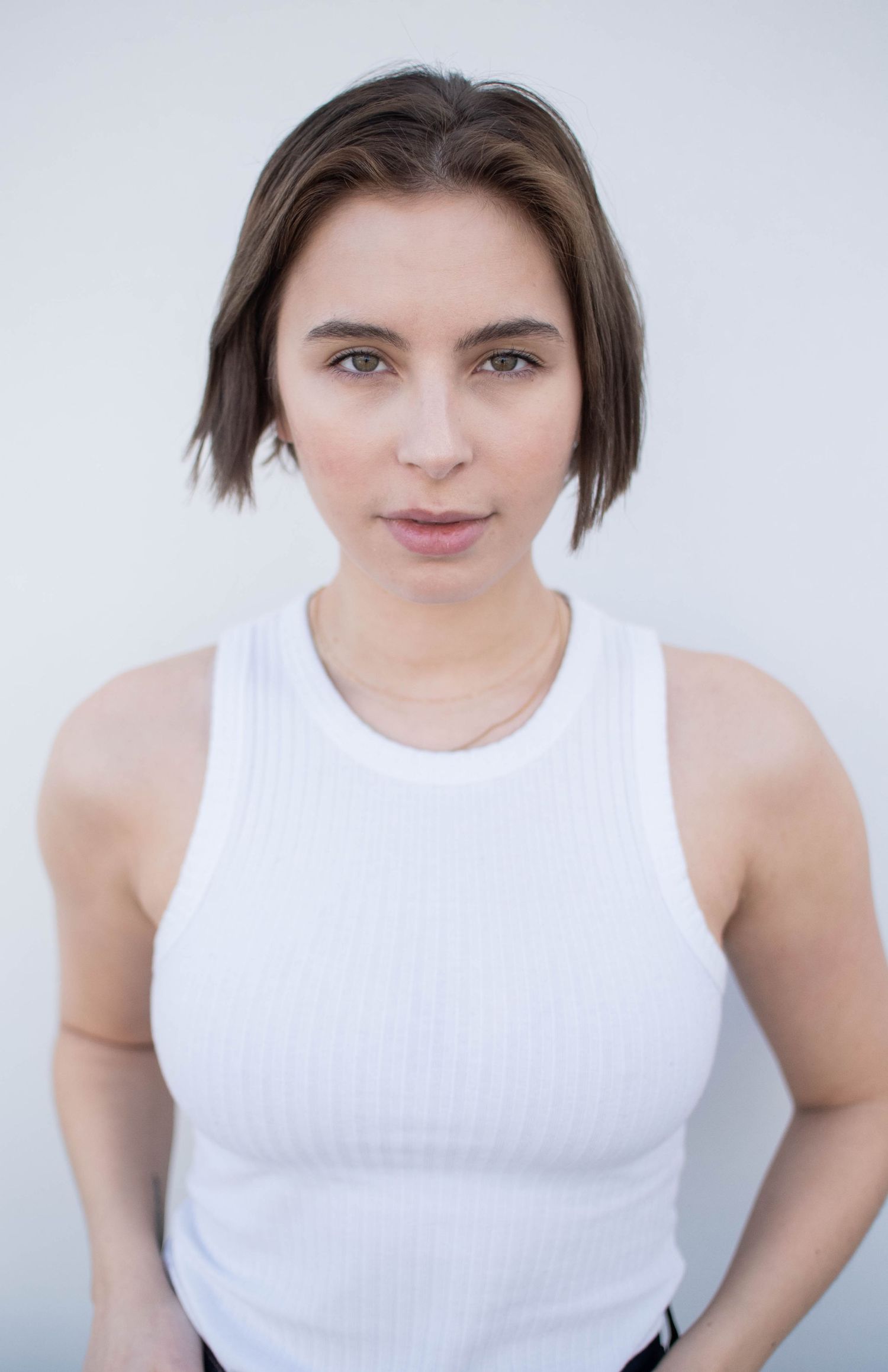 Professional portrait in a white ribbed tank top against a light background.