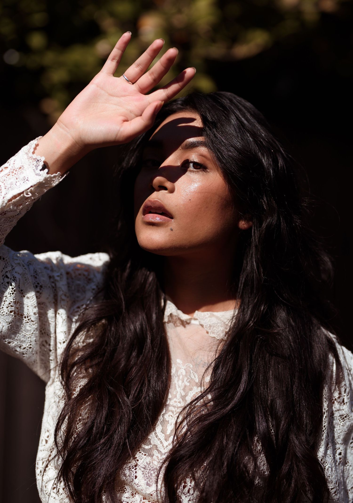 Portrait featuring long dark hair and white lace dress in dramatic sunlight.