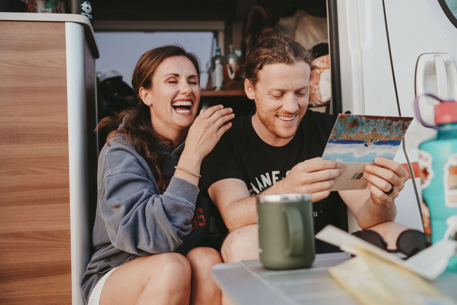 A couple shares a lighthearted moment while having coffee in their camper van.
