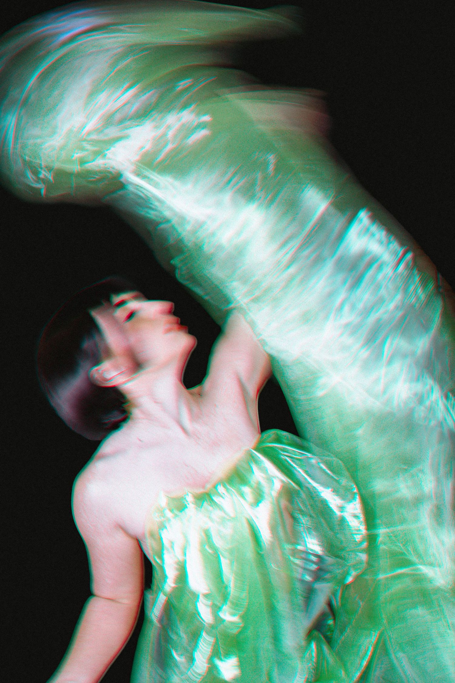 Abstract long exposure photograph showing motion blur in green and pink tones against dark background.