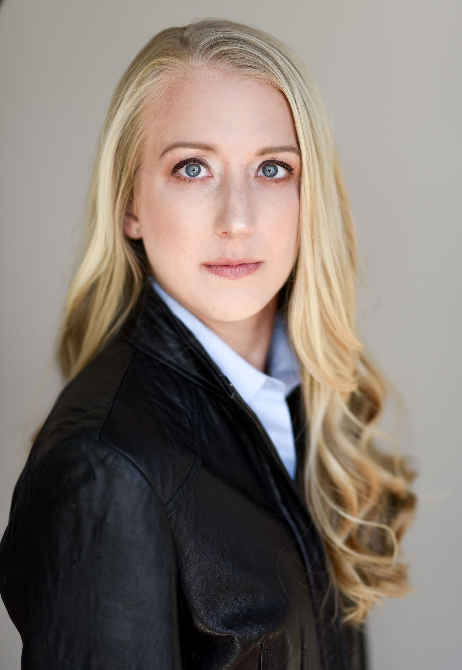 Business portrait in black leather jacket and white collar shirt against neutral background.