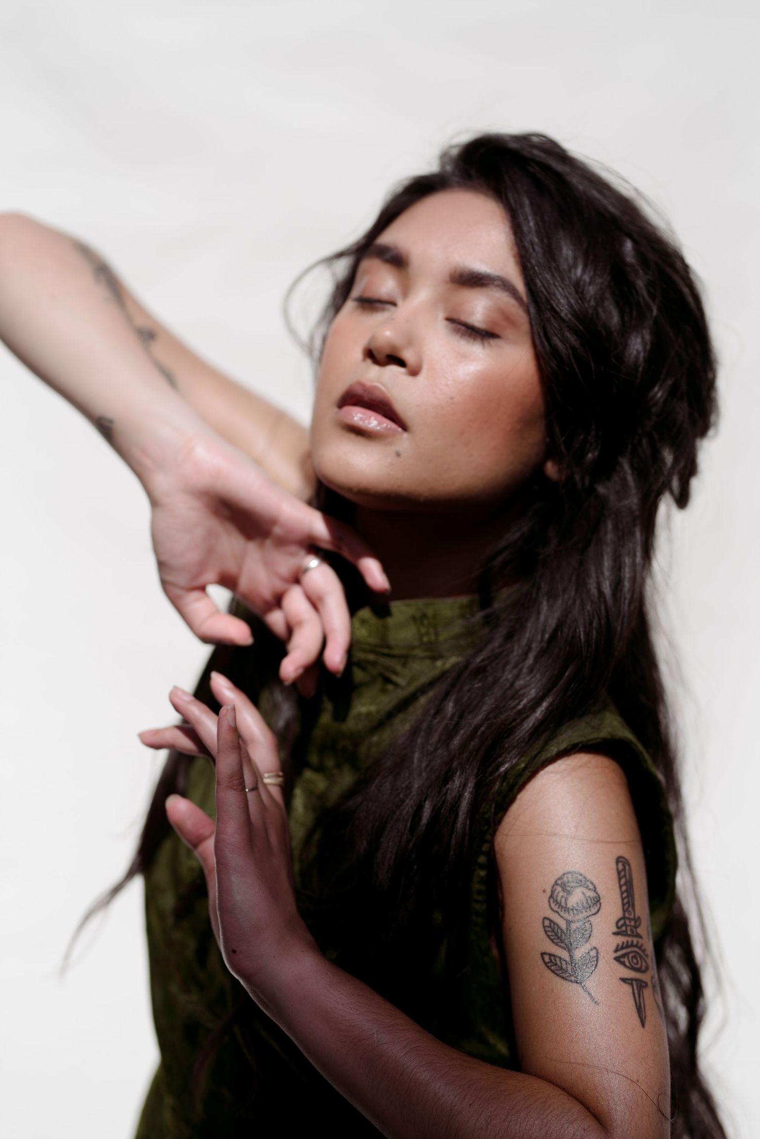Artistic portrait showing graceful hand poses and floral arm tattoo against white background.