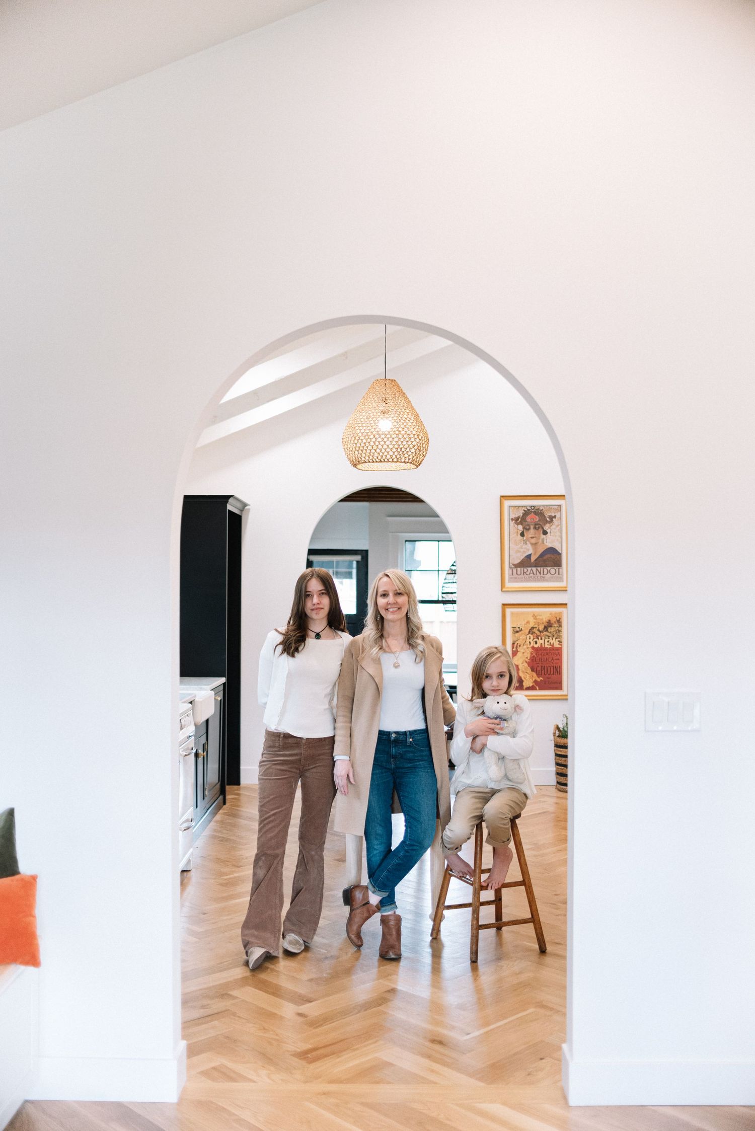 Interior view of a bright modern home with an arched doorway, wooden floors and a hanging woven pendant light.