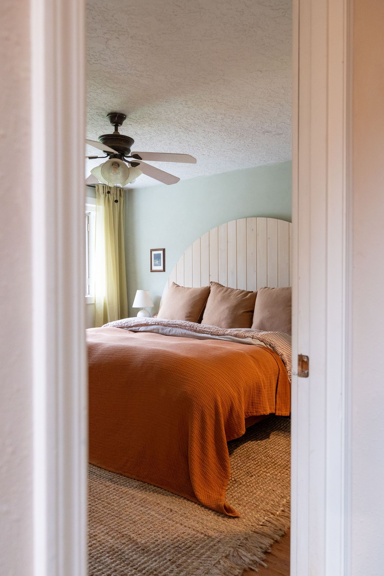 Cozy bedroom with orange blanket and wood paneled headboard viewed through doorway.