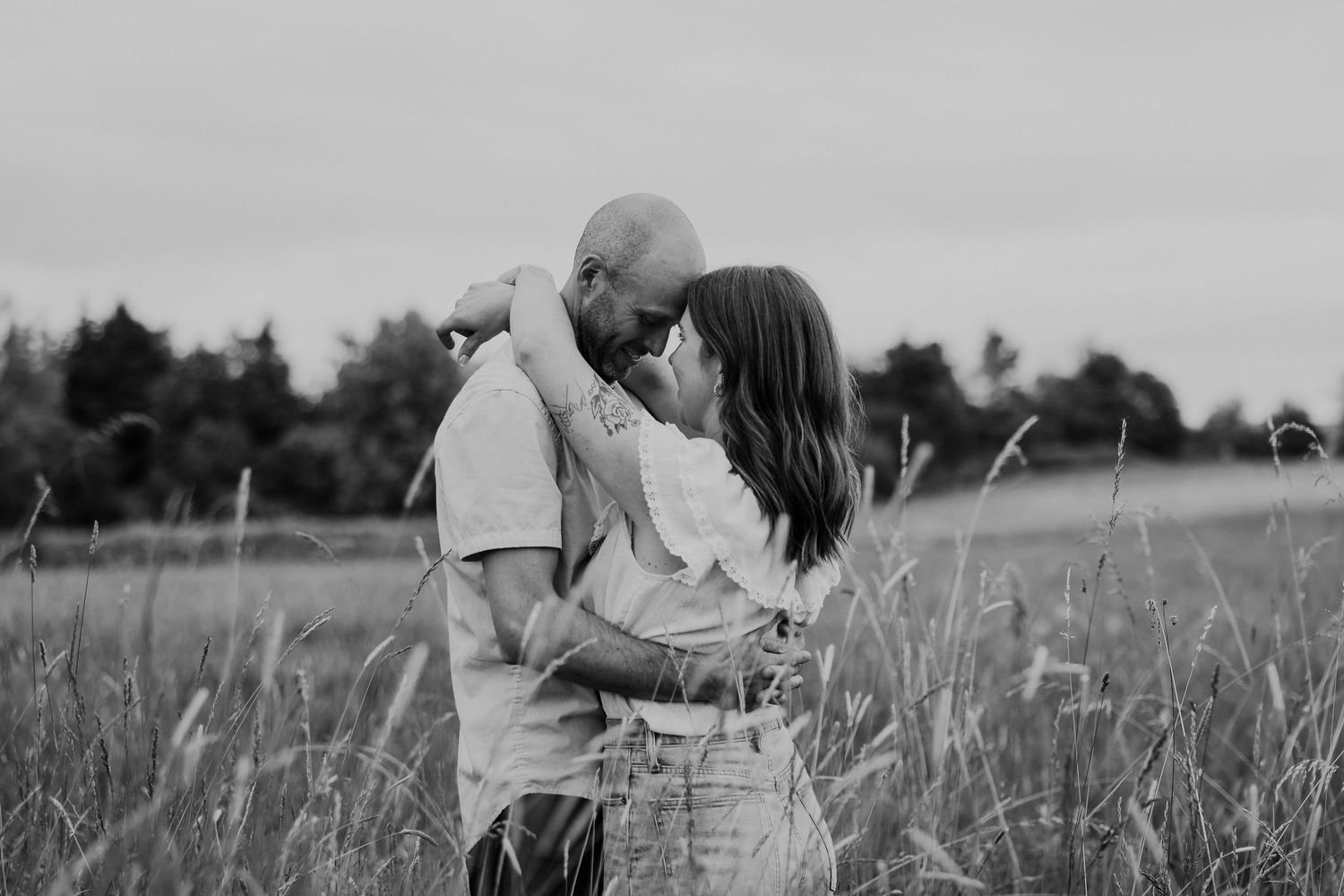 An intimate black and white portrait of a couple embracing in a rustic field.