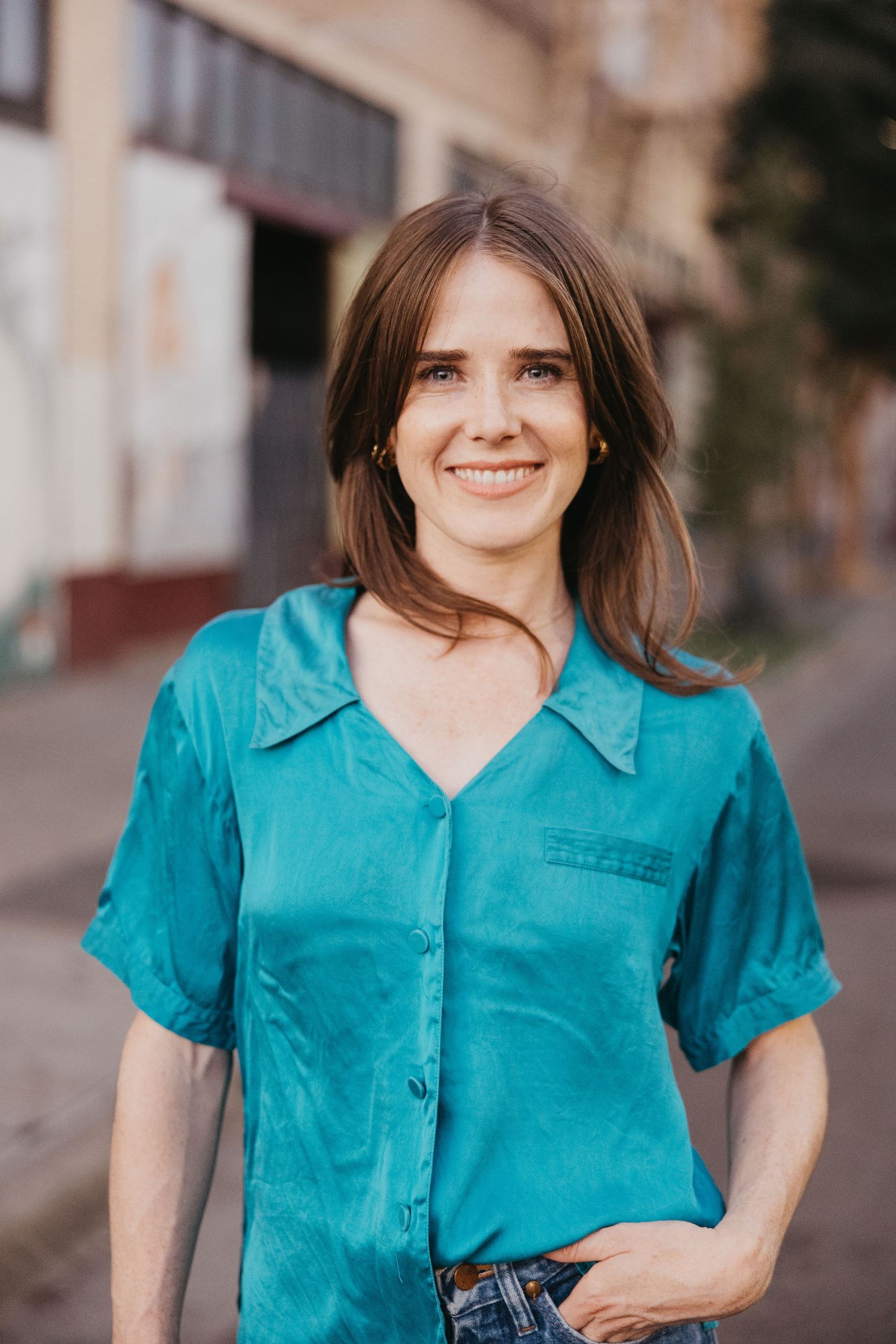 Person in teal button-up shirt smiling outdoors against urban background.
