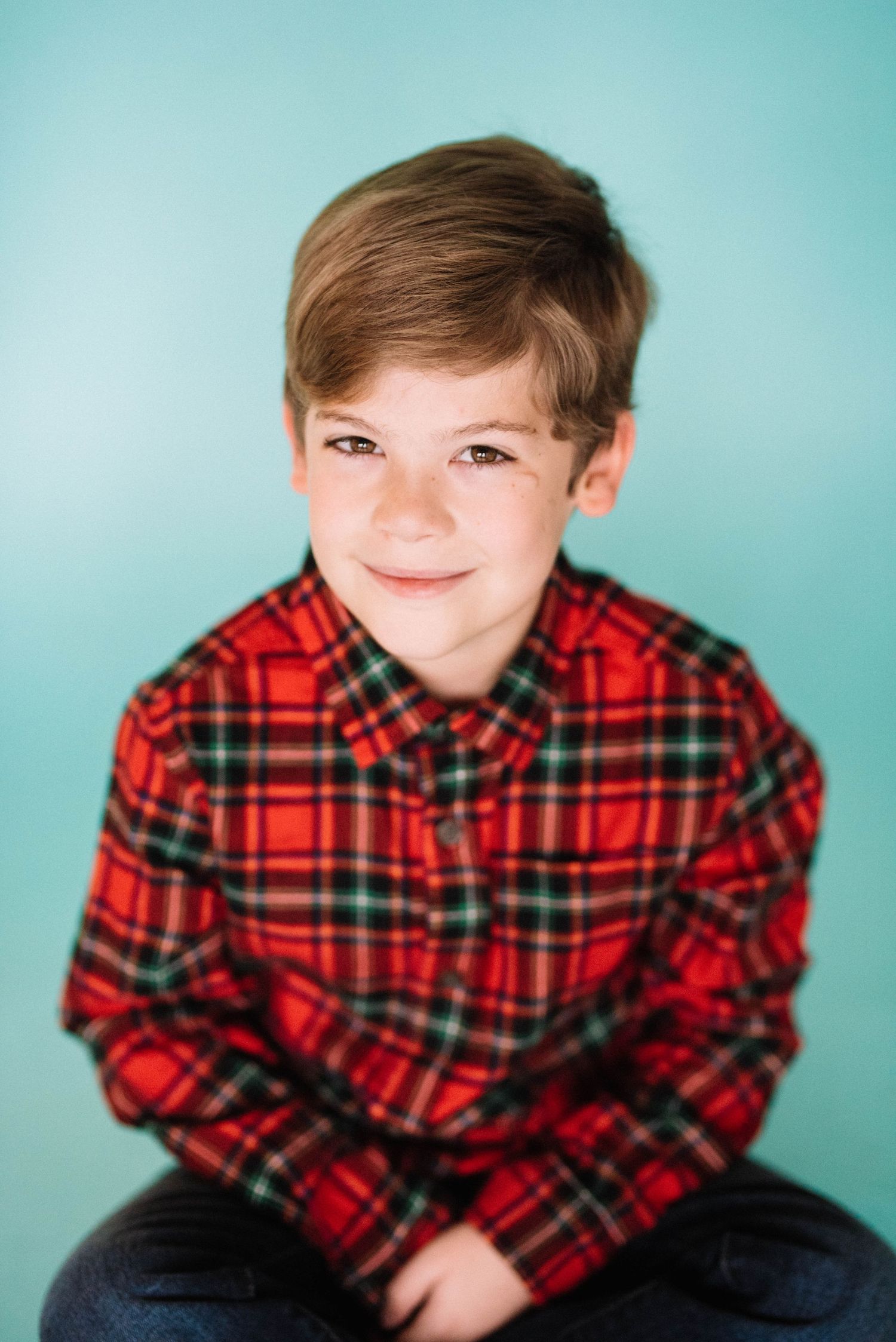 A child in a red plaid flannel shirt poses with various expressions against a blue background.