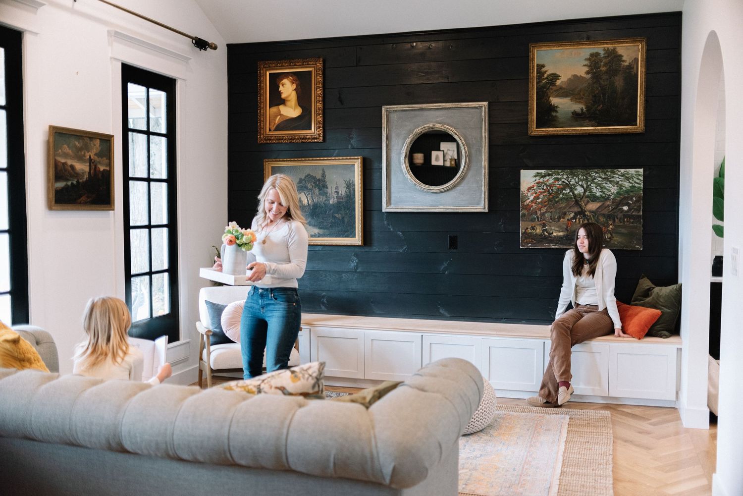 A cozy living room with white sofas, dark walls, and vintage artwork displayed in a gallery wall style.