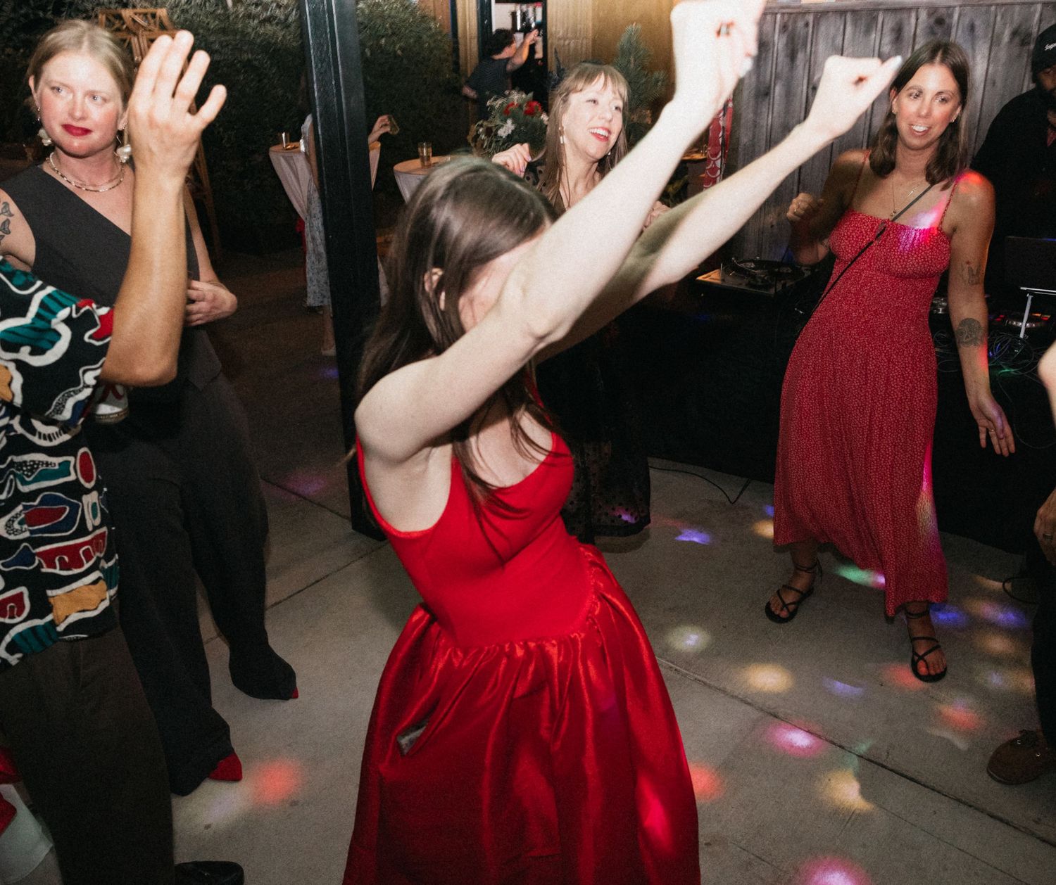 Wedding guests dance and celebrate on a dimly lit dance floor with colorful lighting effects.