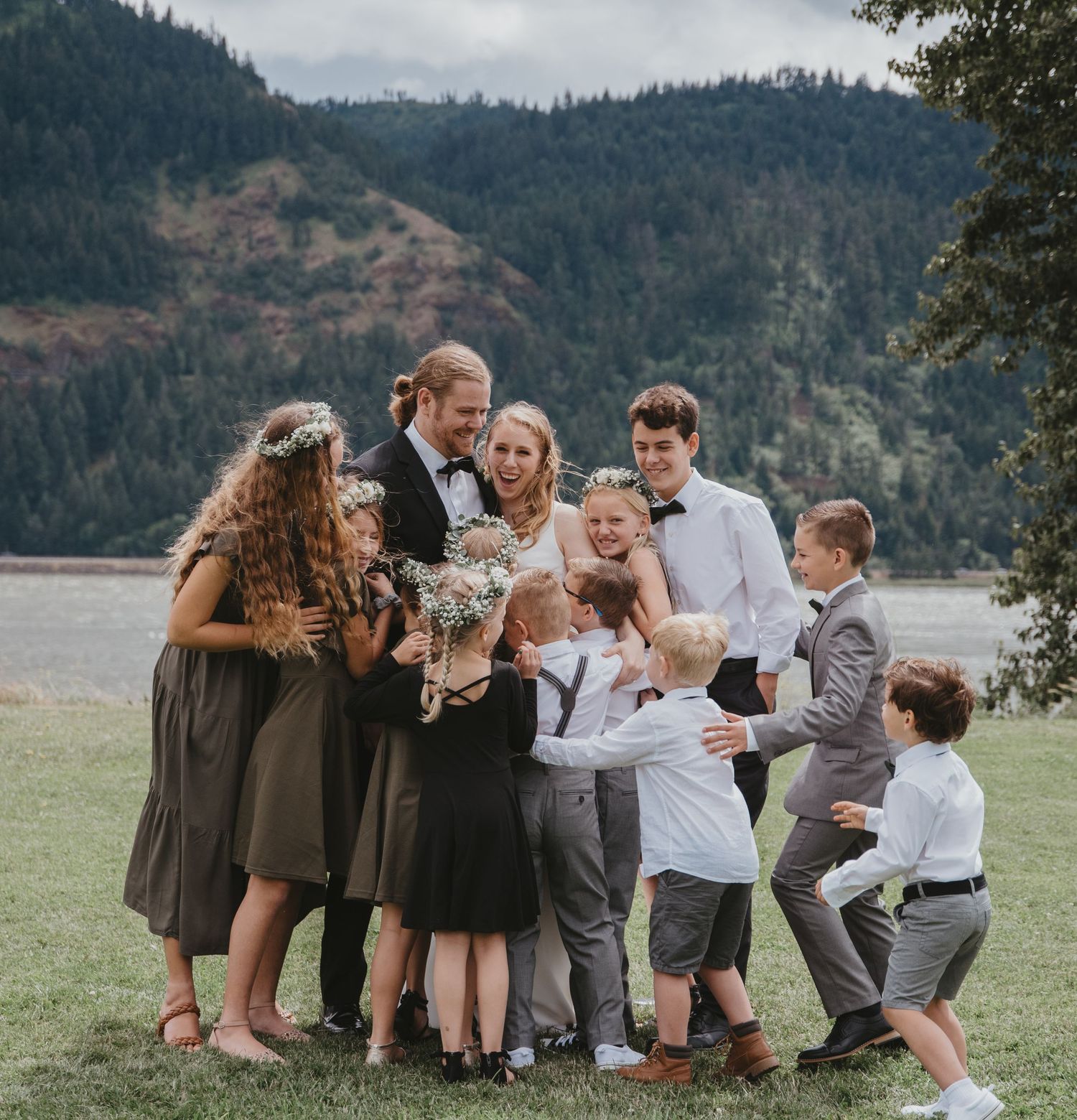 A joyful group gathering outdoors with mountain and lake scenery in the background.