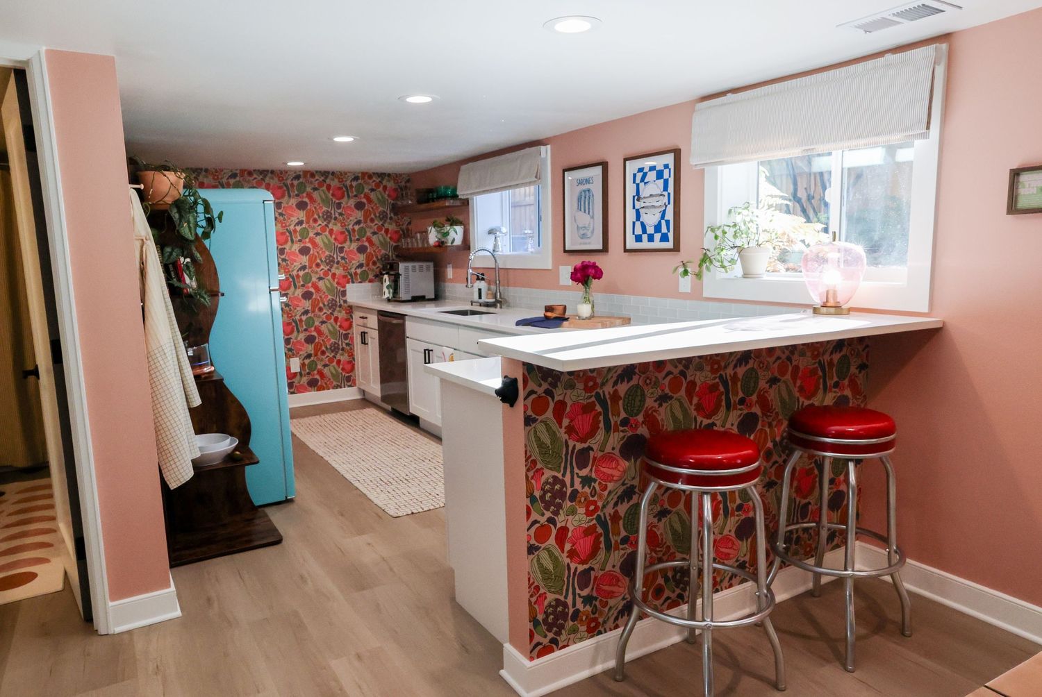 Retro-styled kitchen with red floral wallpaper, bar stools, and white countertops.