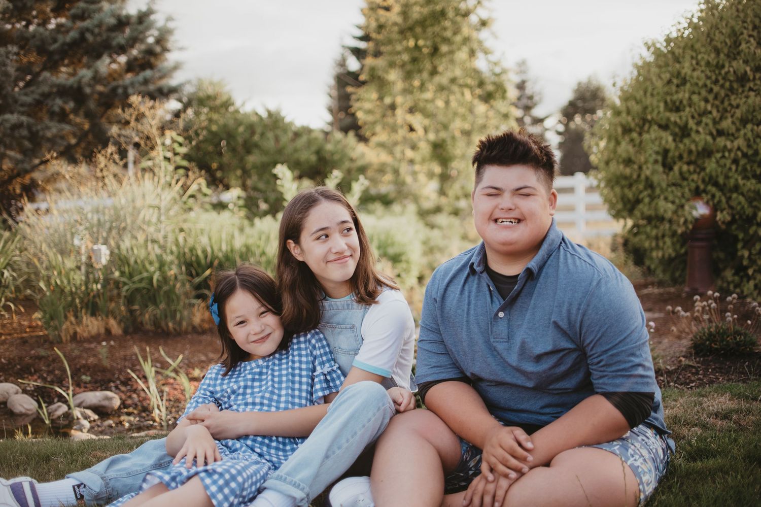Family members sit together on grass during an outdoor photo session in a natural setting at sunset.