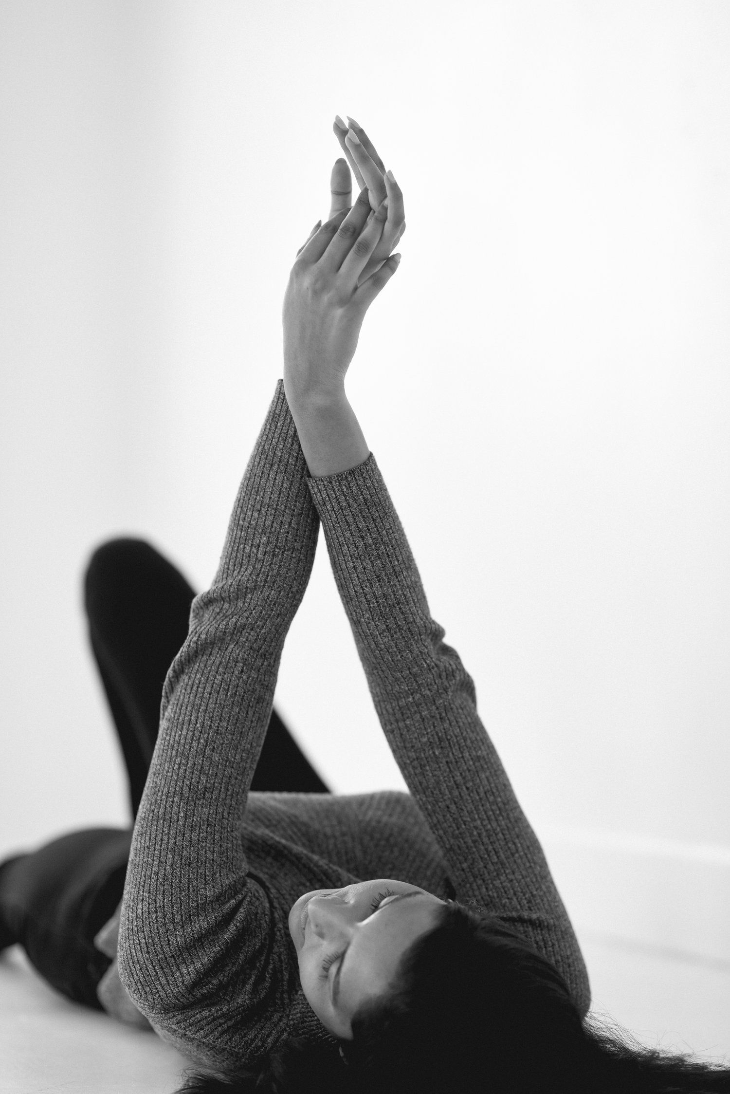 Black and white photo of someone lying down with raised hands in knit sweater.
