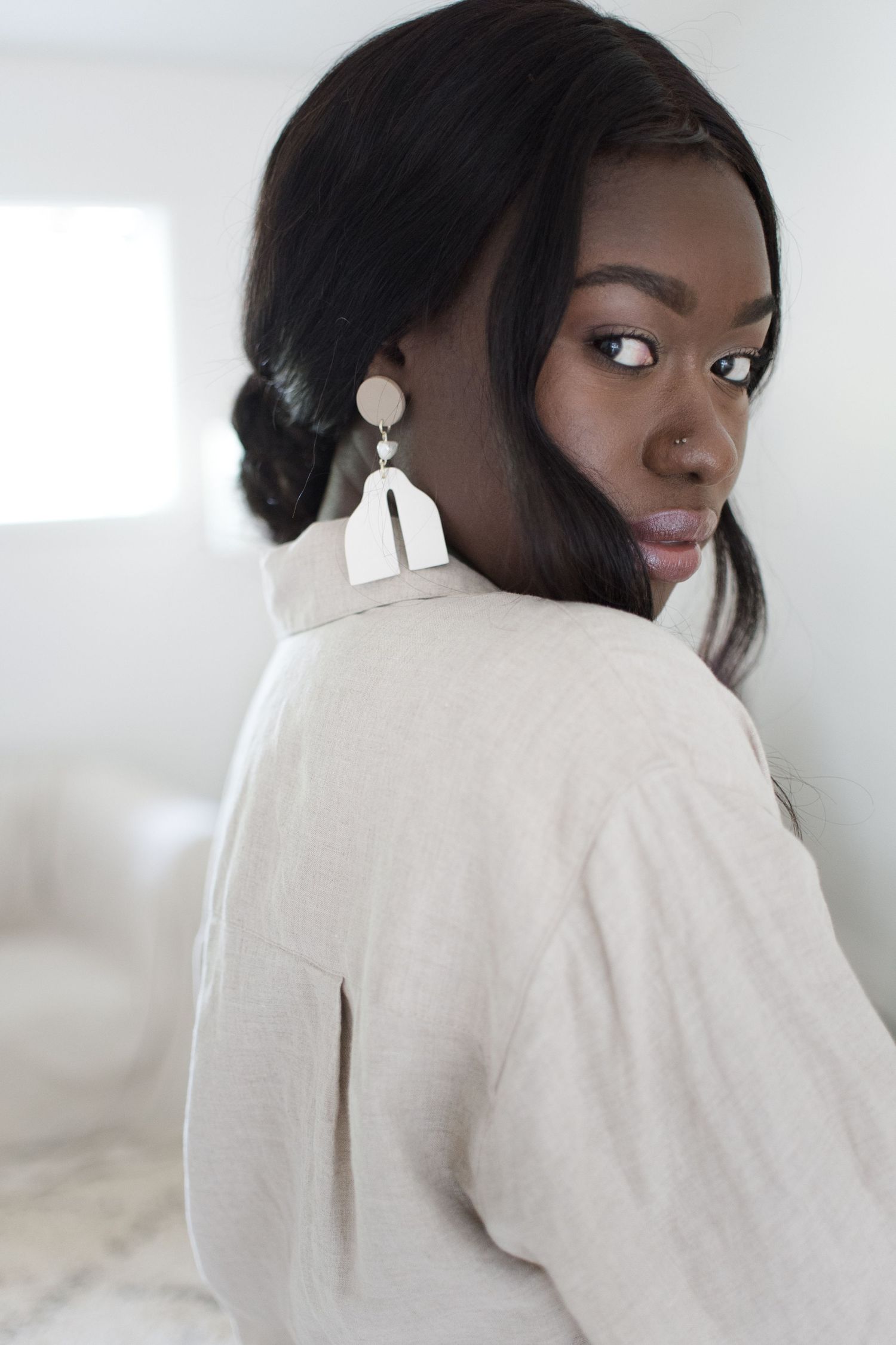 Elegant portrait showing silver statement earrings and white collared shirt in bright interior.