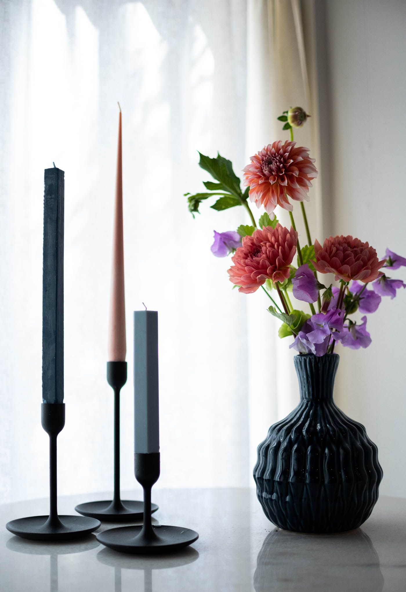 Elegant black decorative vase with pink dahlias and purple flowers next to three tall black and pink candlesticks.