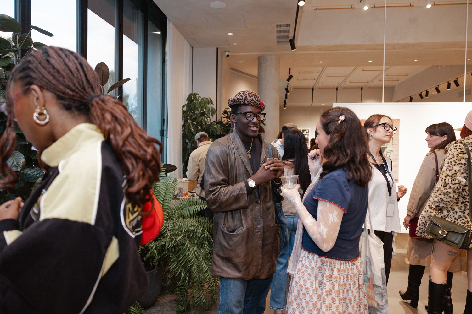 People gathered in a gallery space viewing and discussing artwork at an exhibition opening.