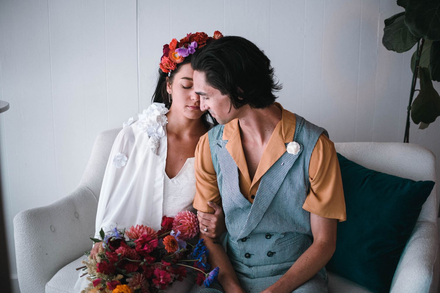 Two people sharing an intimate moment on a couch surrounded by vibrant flowers.