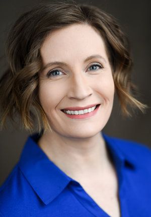 Professional headshot of a person in a bright blue top with short wavy hair against dark background.