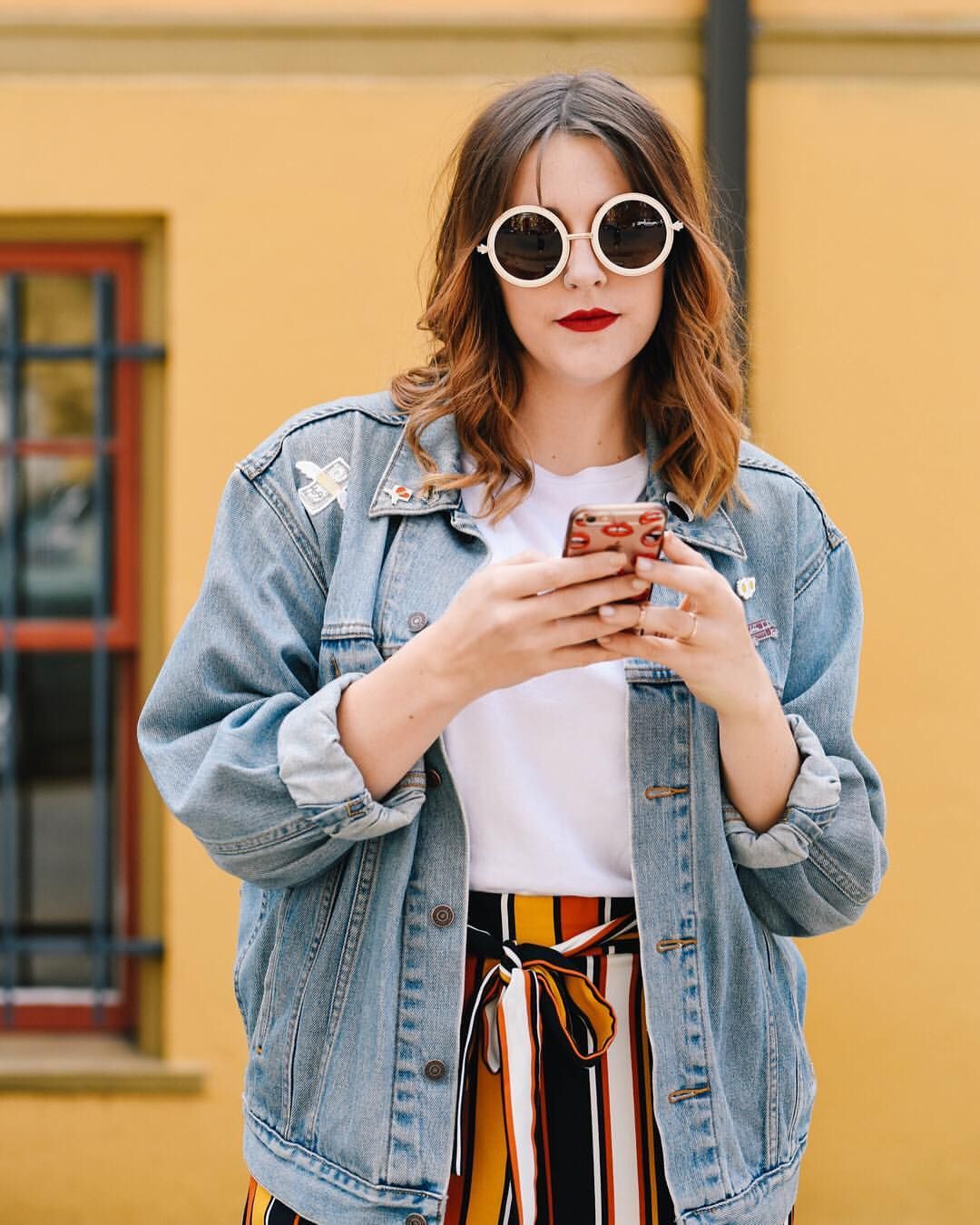Stylish street fashion with denim jacket and round sunglasses against yellow wall.