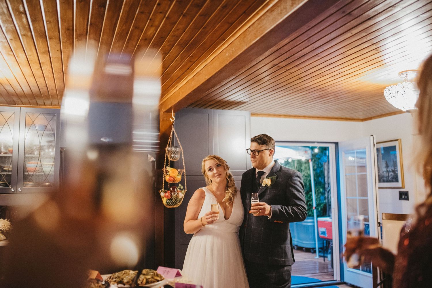 A bride and groom toast at their wedding reception under wooden ceiling panels.