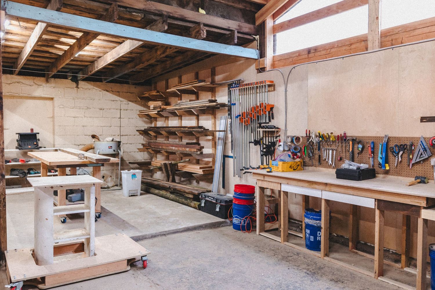 Well-organized woodworking workshop with lumber storage racks and workbench filled with tools and equipment.