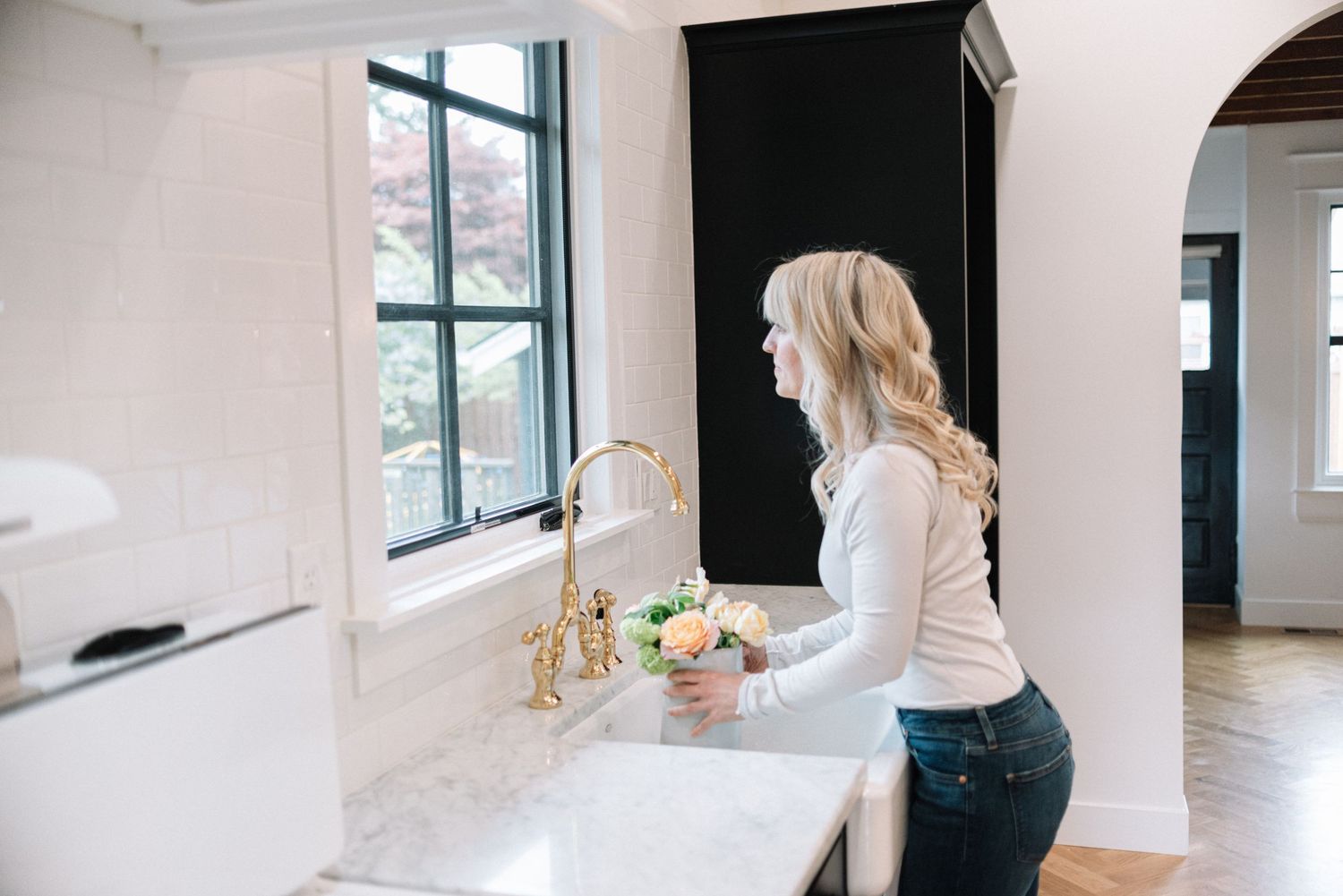 Woman washing dishes at a modern white farmhouse sink with gold faucet.