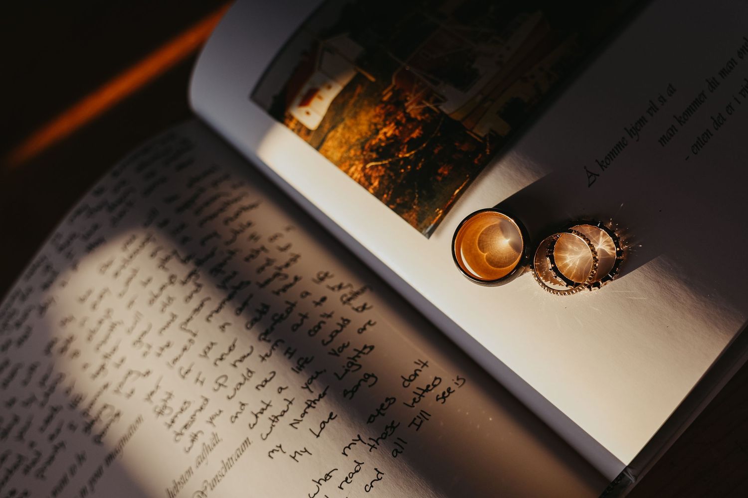Wedding rings rest on handwritten vows in dramatic lighting.