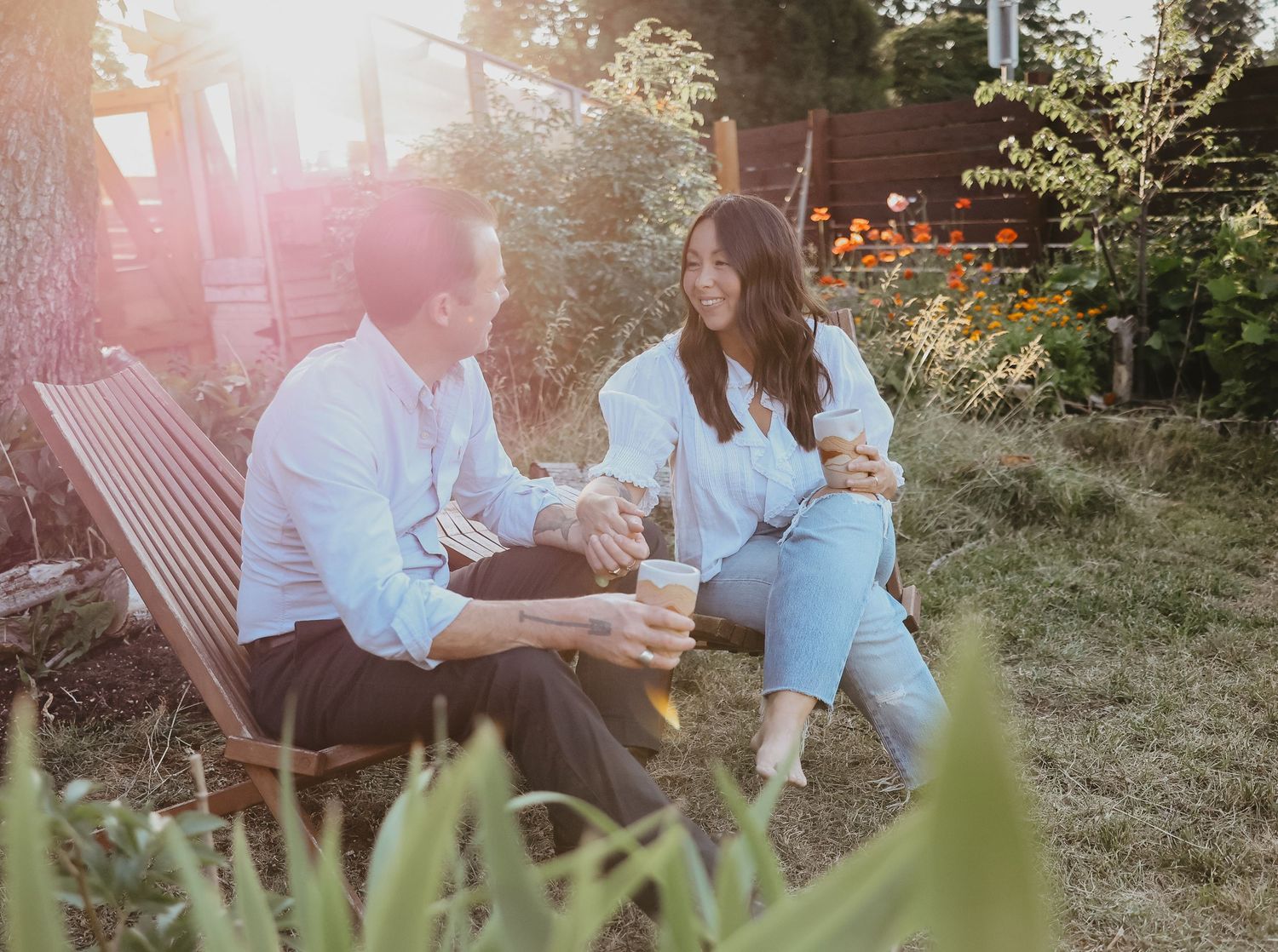 A couple enjoys a relaxed evening moment together on garden furniture at sunset.