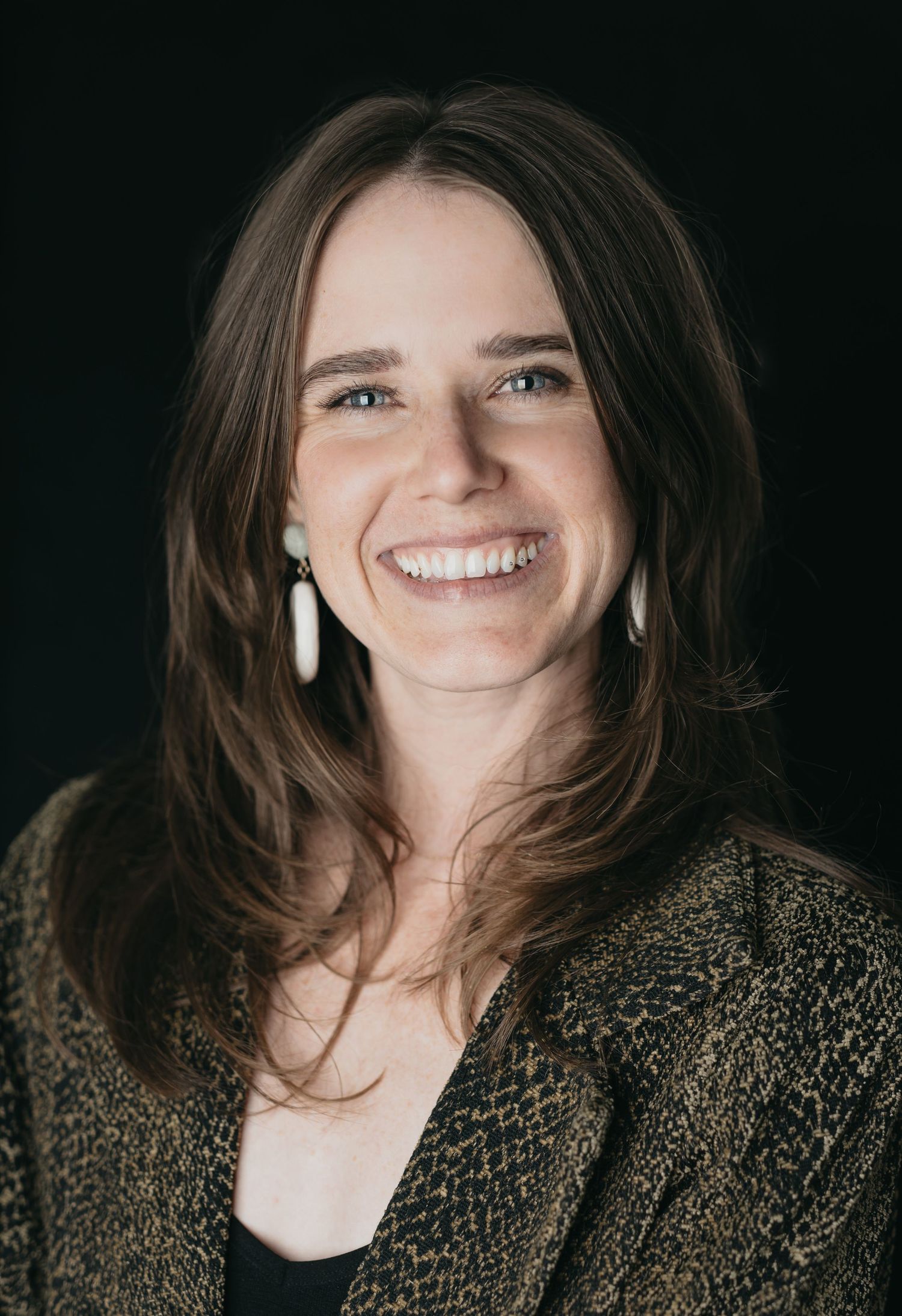 Professional portrait of someone in a dark sweater with a warm smile against a black background.