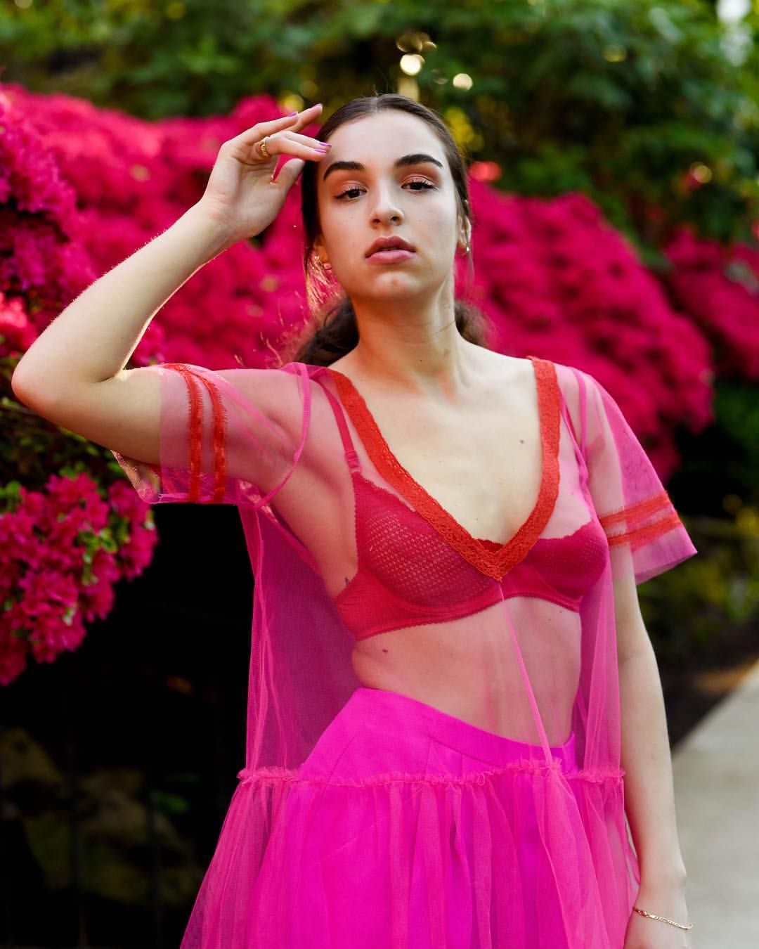 Fashion portrait in flowing pink sheer dress against vibrant magenta flowers.