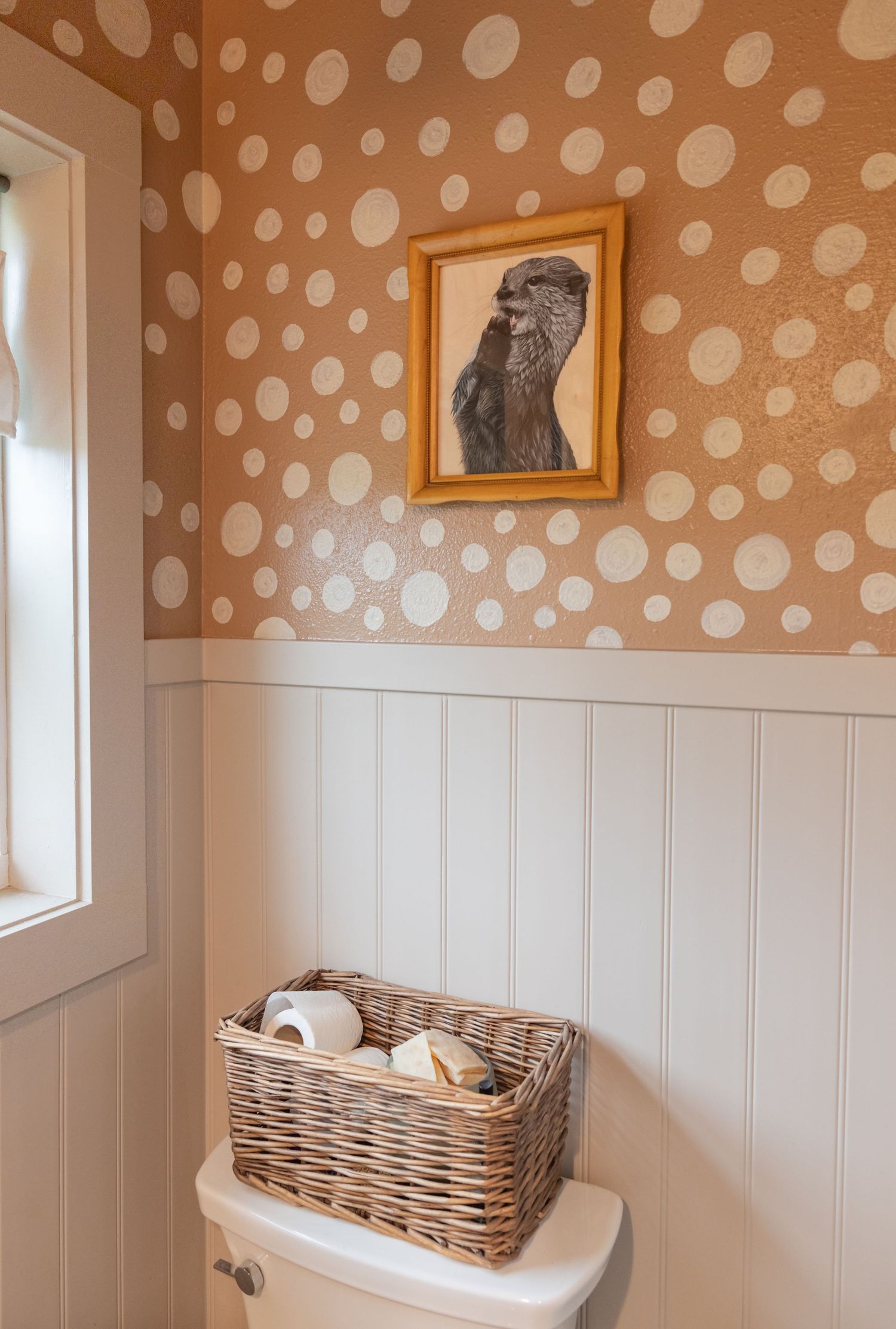 Polka dot wallpaper bathroom with white wainscoting and framed dog portrait.