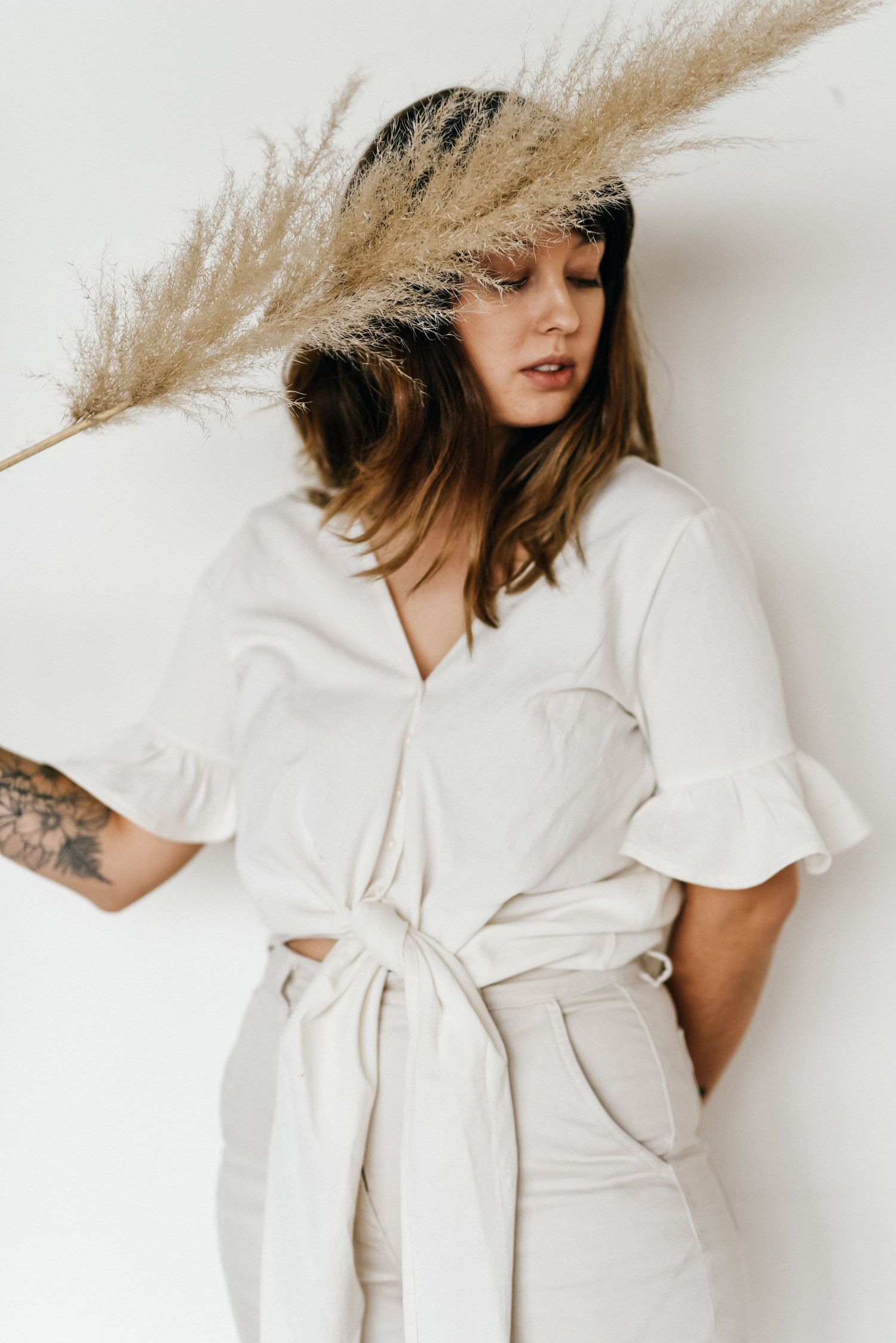 Artistic portrait with pampas grass featuring white tied dress and natural styling.
