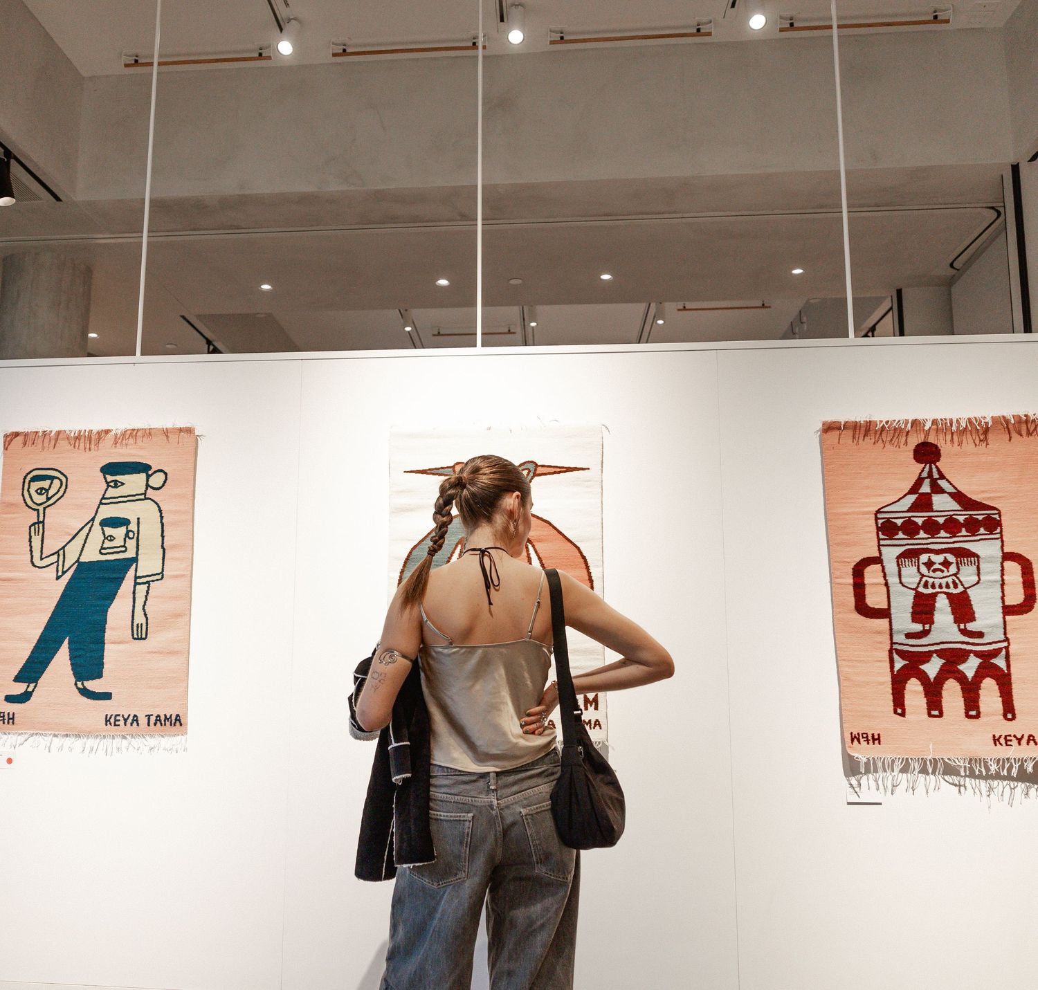Art gallery visitors examine artwork displayed on white walls with track lighting overhead.
