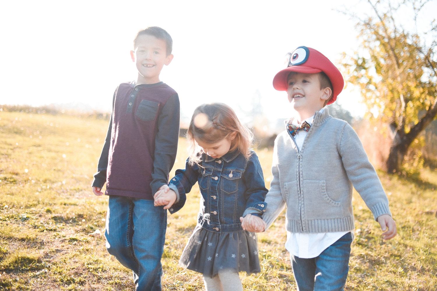 Three young children walk together through a golden field during sunset.