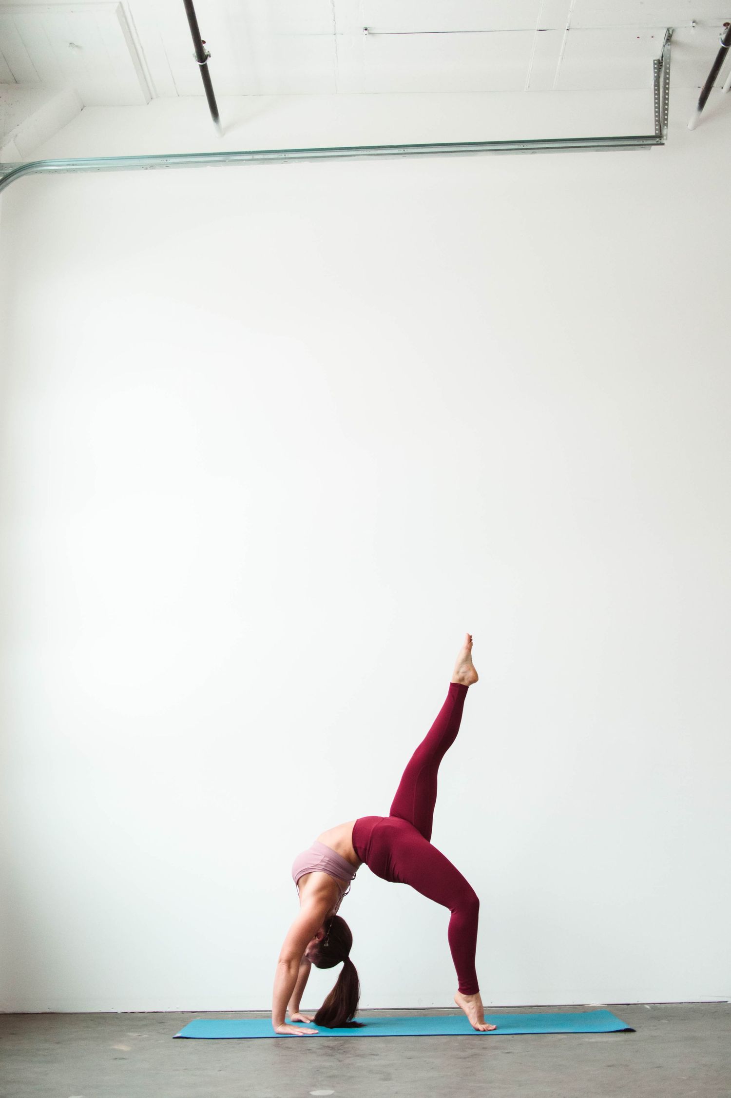 Person in burgundy workout attire performing wheel pose on blue yoga mat.