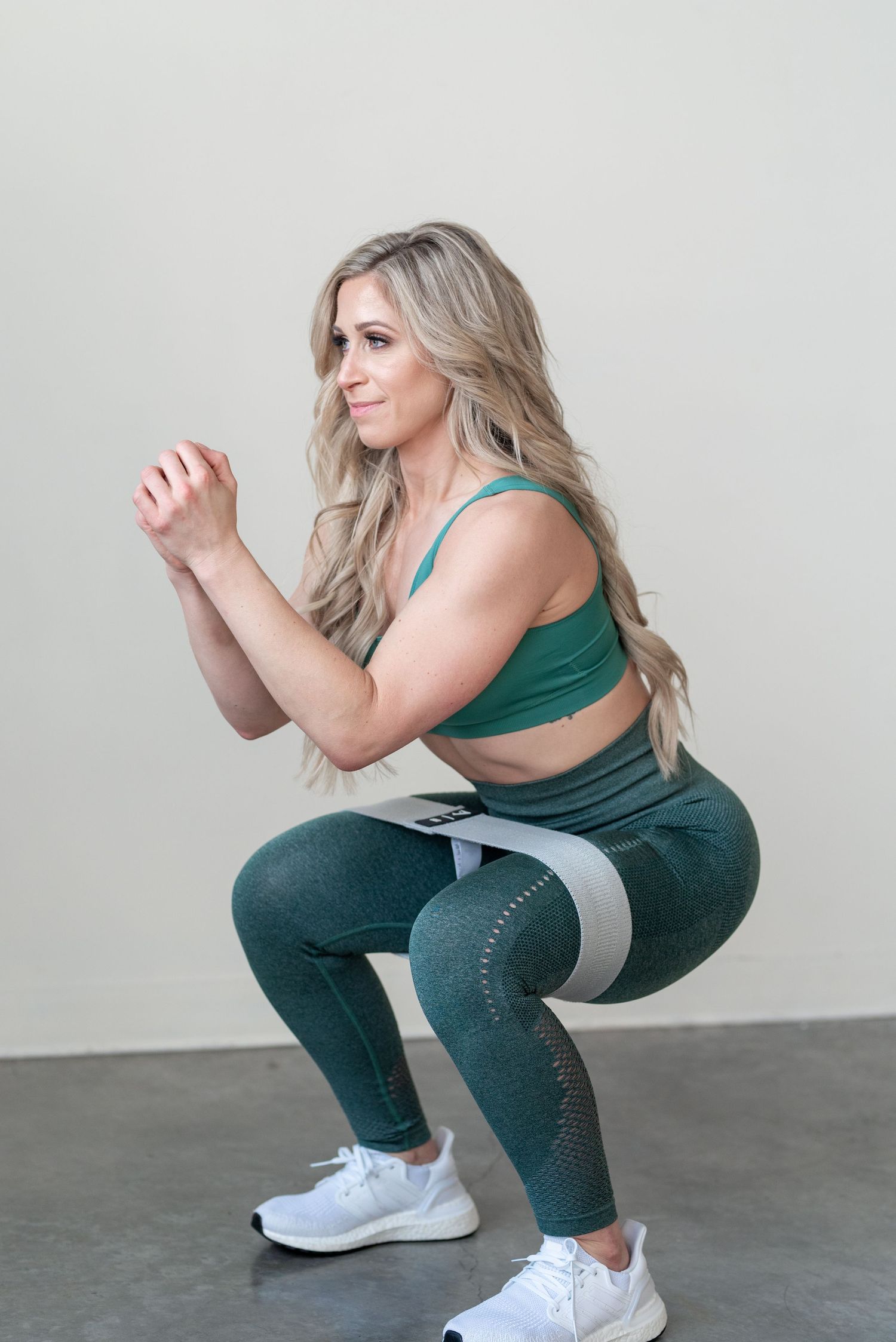 Resistance band squat exercise demonstrated in green athletic wear on concrete floor.