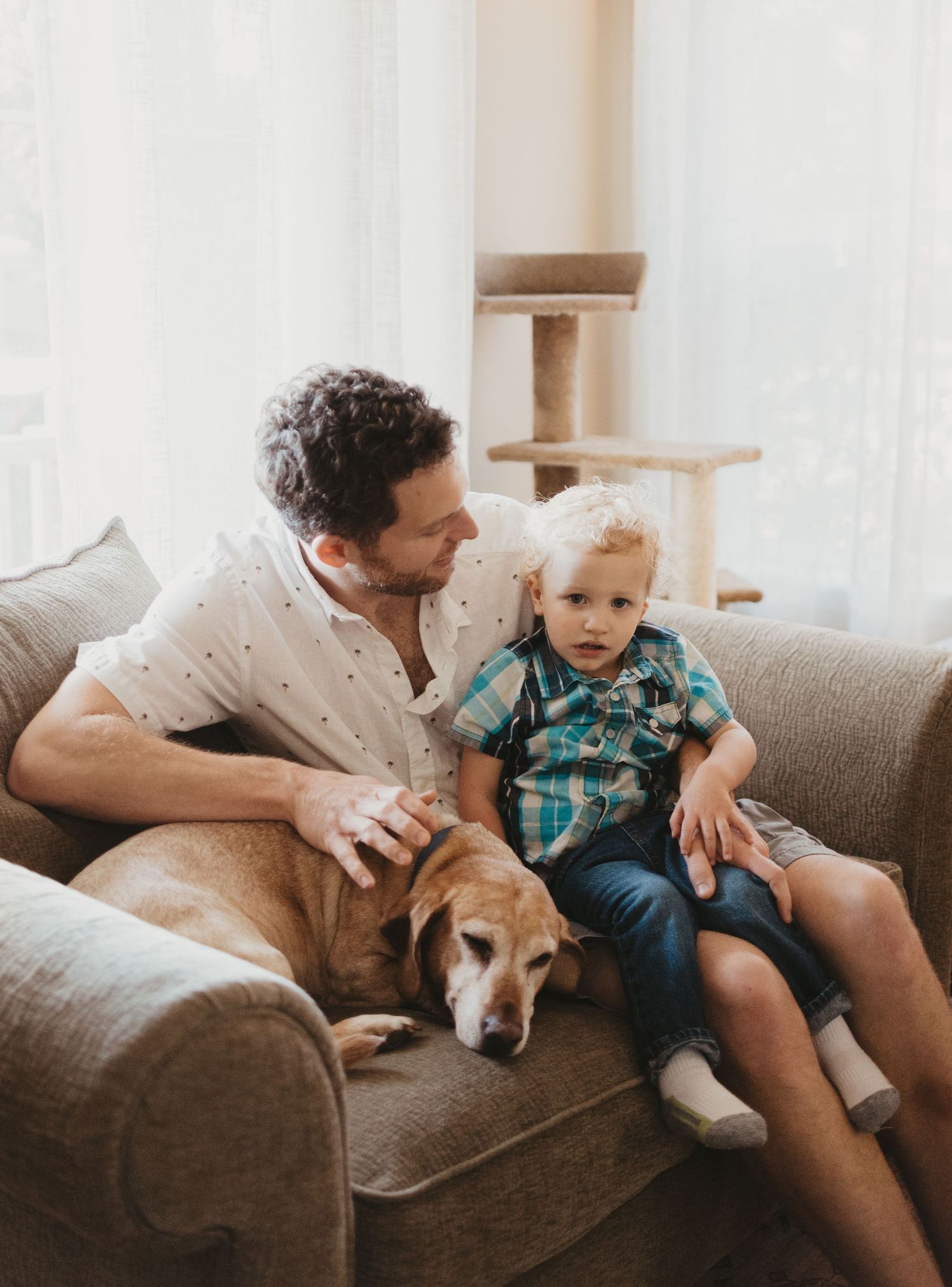 A relaxed family moment on the couch with a sleeping dog and toddler in plaid.