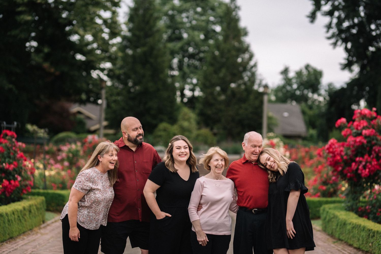 Multi-generational family portrait in garden with blooming red flowers.