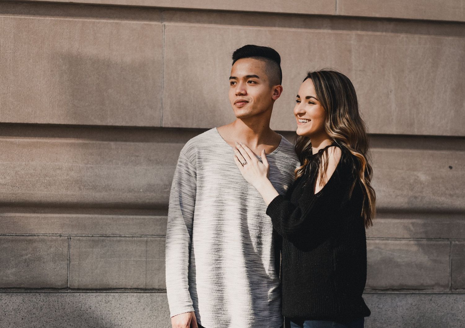 Young couple in casual clothing standing against concrete wall in urban setting.