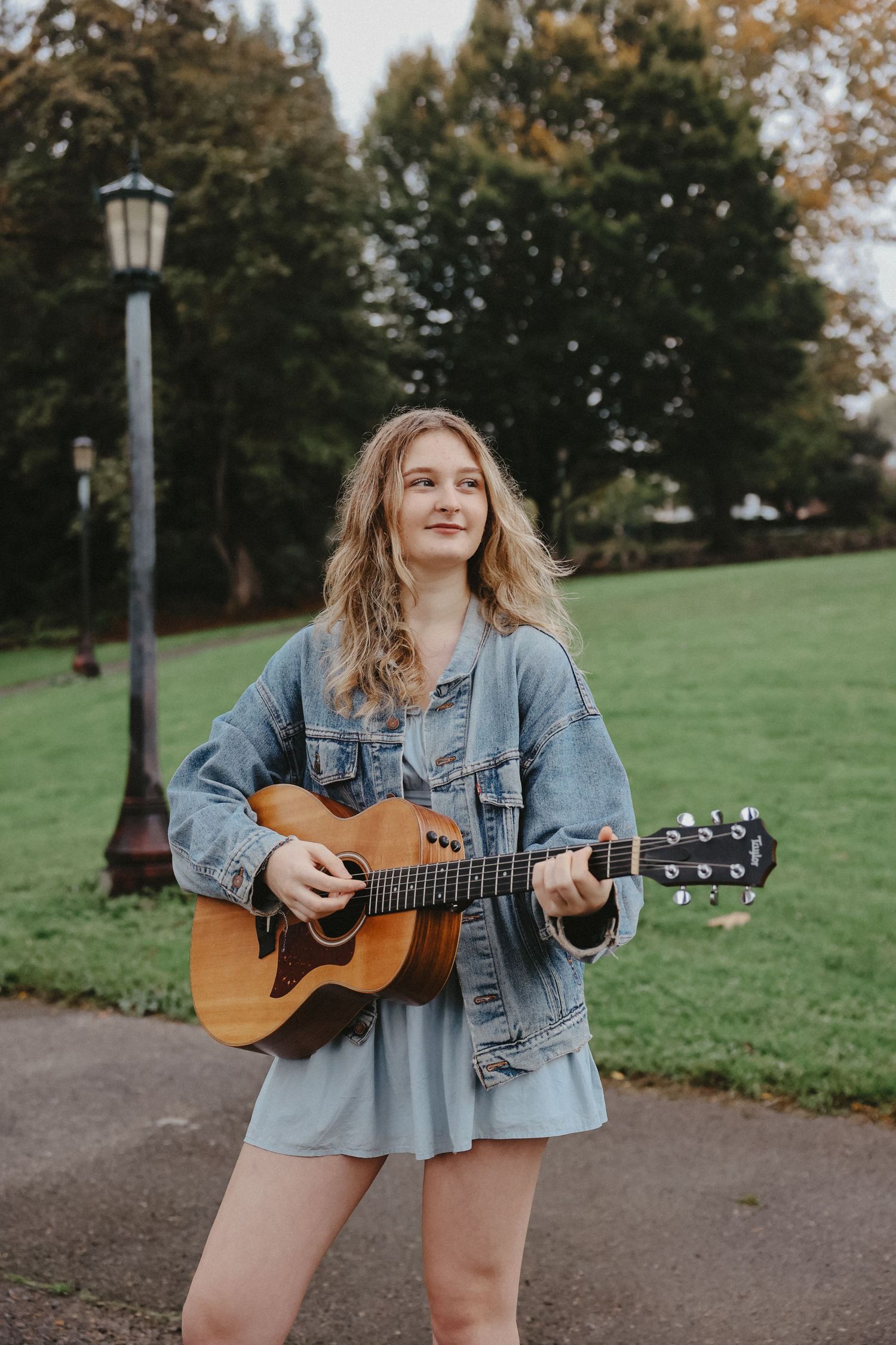 Musician playing acoustic guitar on park path with autumn scenery.