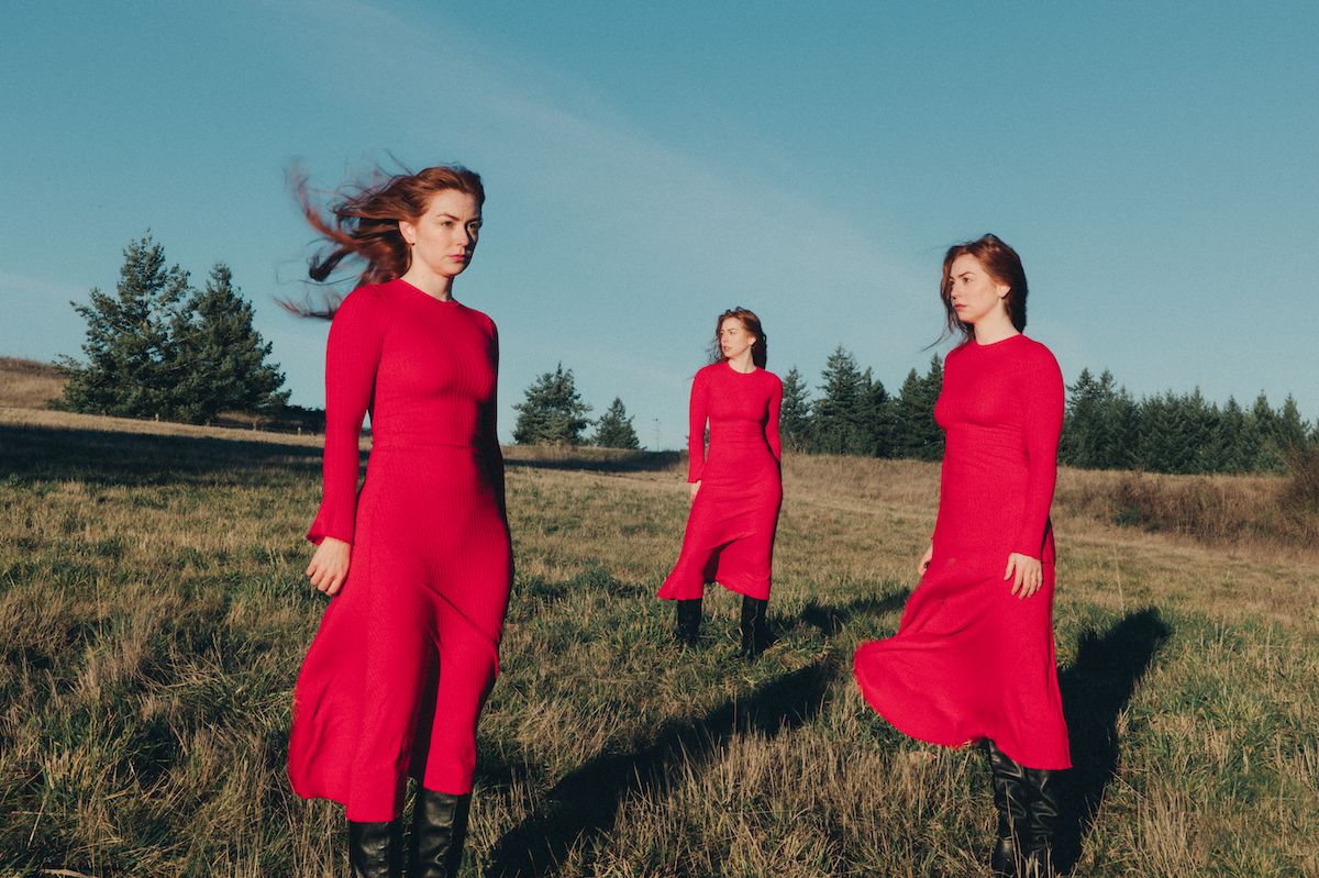 A sequence of figures in bright red sweaters moving across a grassy hilltop against a blue sky.