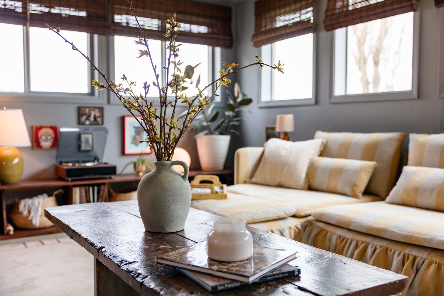 Cozy living room with beige sofa, rustic coffee table, and flowering branches in a gray ceramic vase.