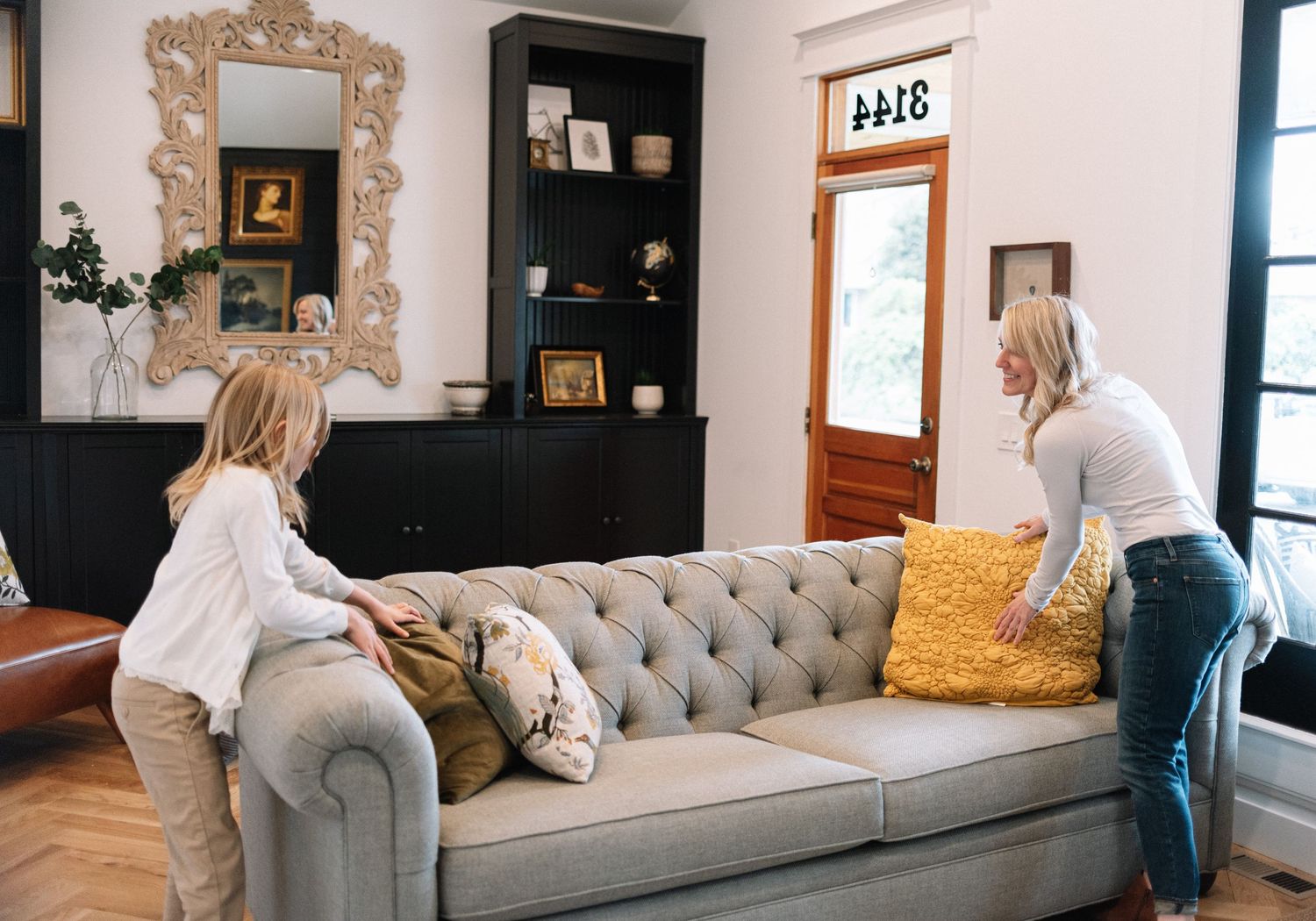 Cozy living room with grey tufted sofa, ornate mirror, and black built-in shelving.