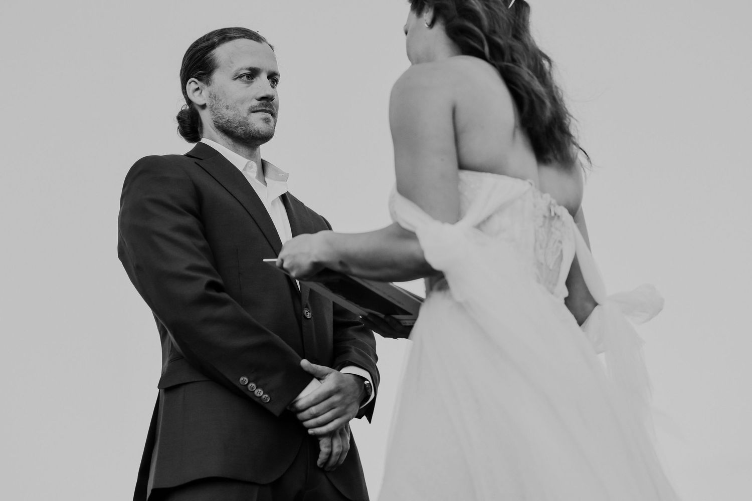 A tender pre-wedding moment between two people in formal attire, captured in black and white.
